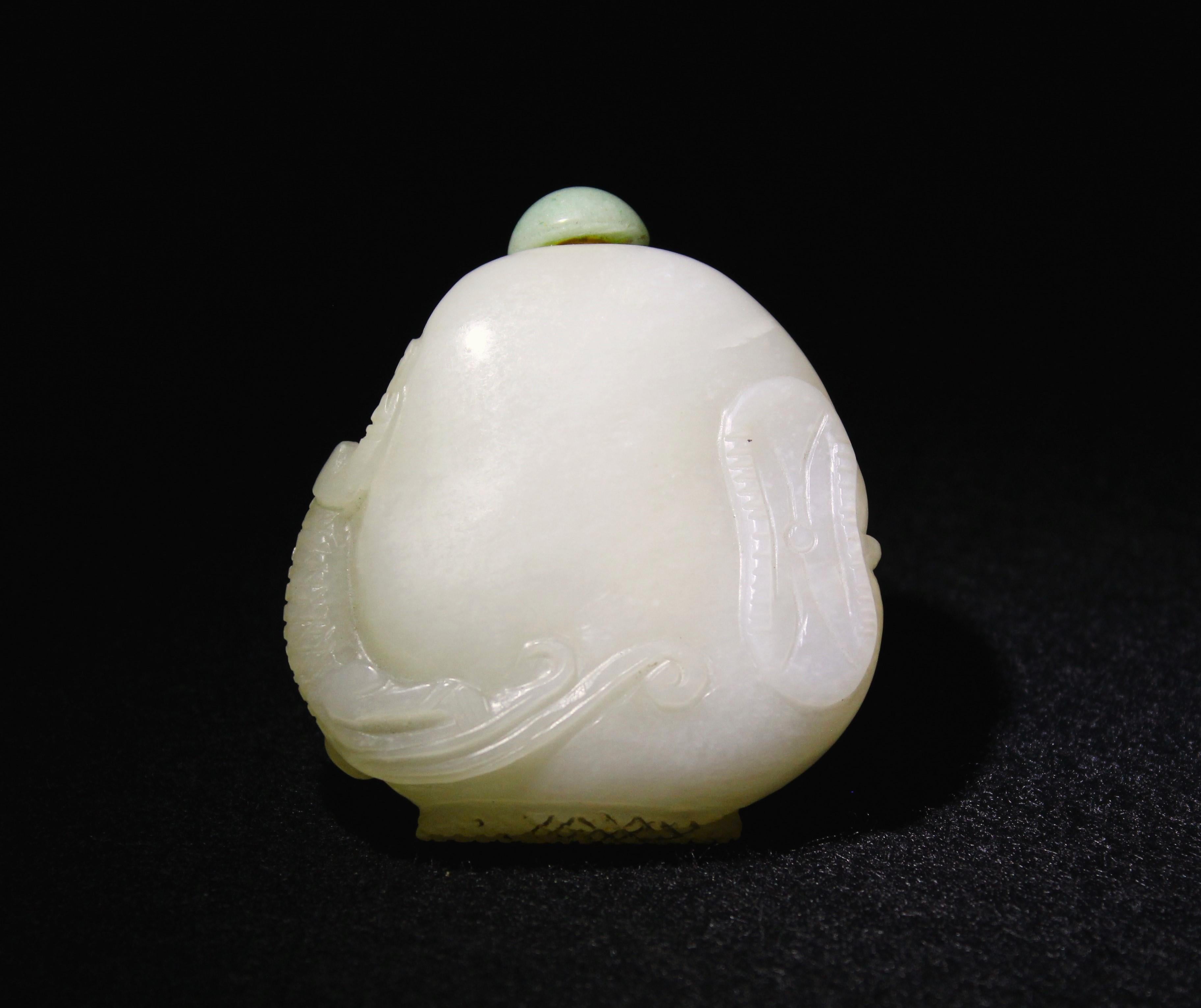 A masterfully carved white jade snuff bottle, showcasing a sinuous chilong grasping a lotus/lingzhi vein, elegantly draping down to a lotus seed bud at the base. The opposite side features a delicate lotus leaf, balancing the composition with subtle