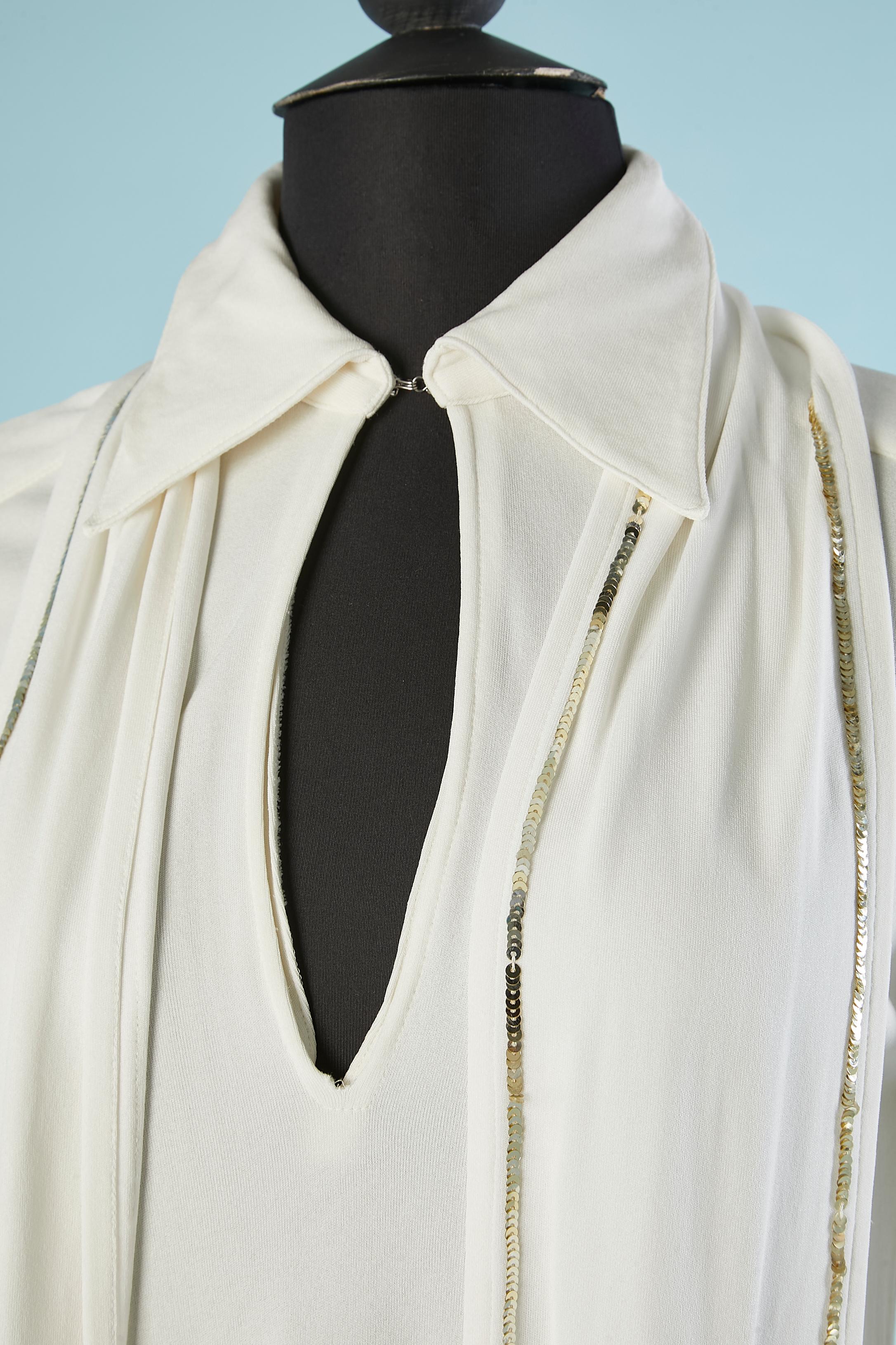 White jersey tunic.  Scarf with gold sequins edge ( can be also wear as belt)  Hook& eye on the top middle front. Cut-work on the shoulders. Transparent plastic snaps on the cuffs. Split on both side. 
Size of  of the scarf ( or belt) = 220cm X