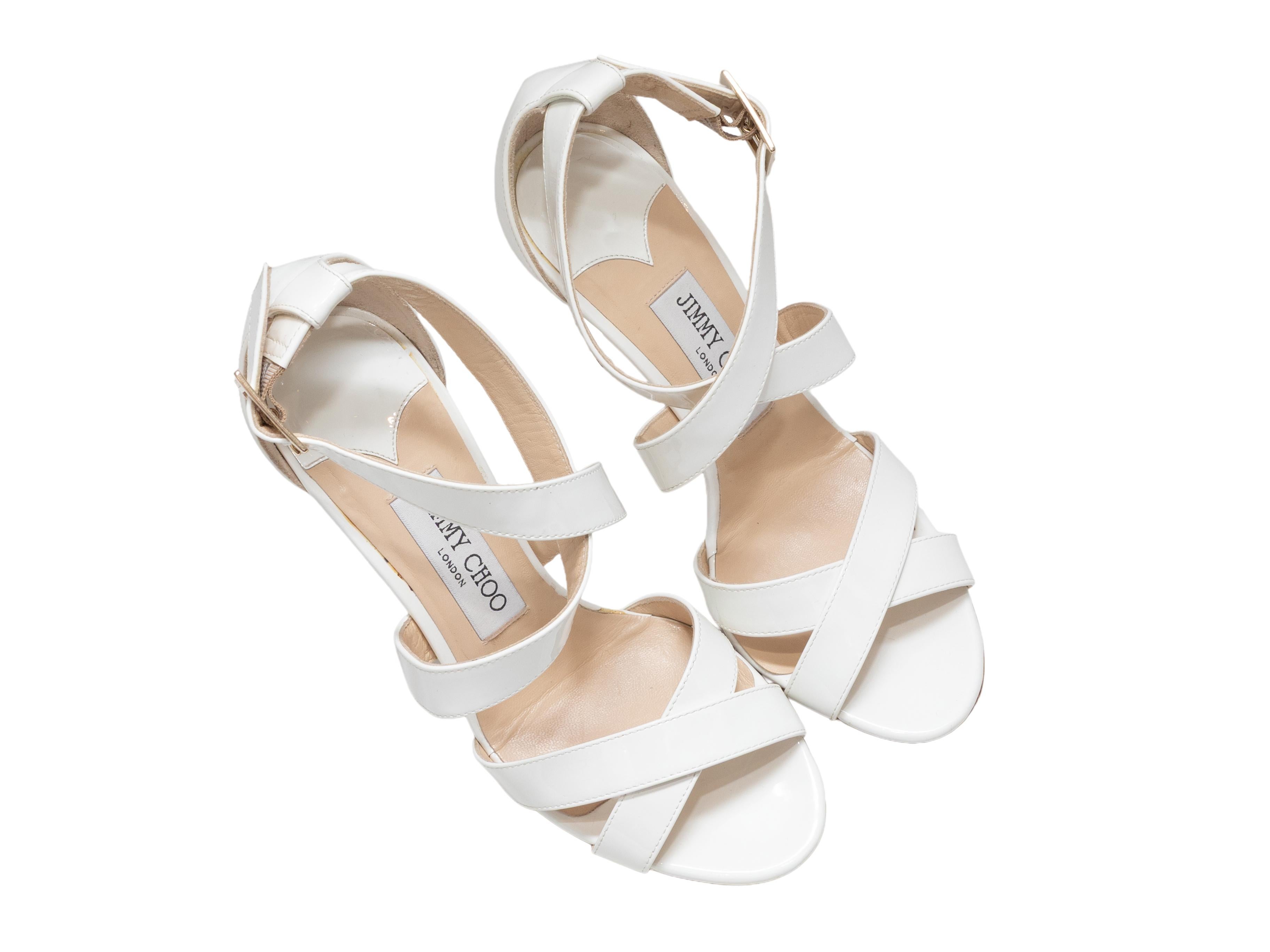 White patent leather heeled sandals by Jimmy Choo. Gold-tone buckle closures at ankle straps. 4.15