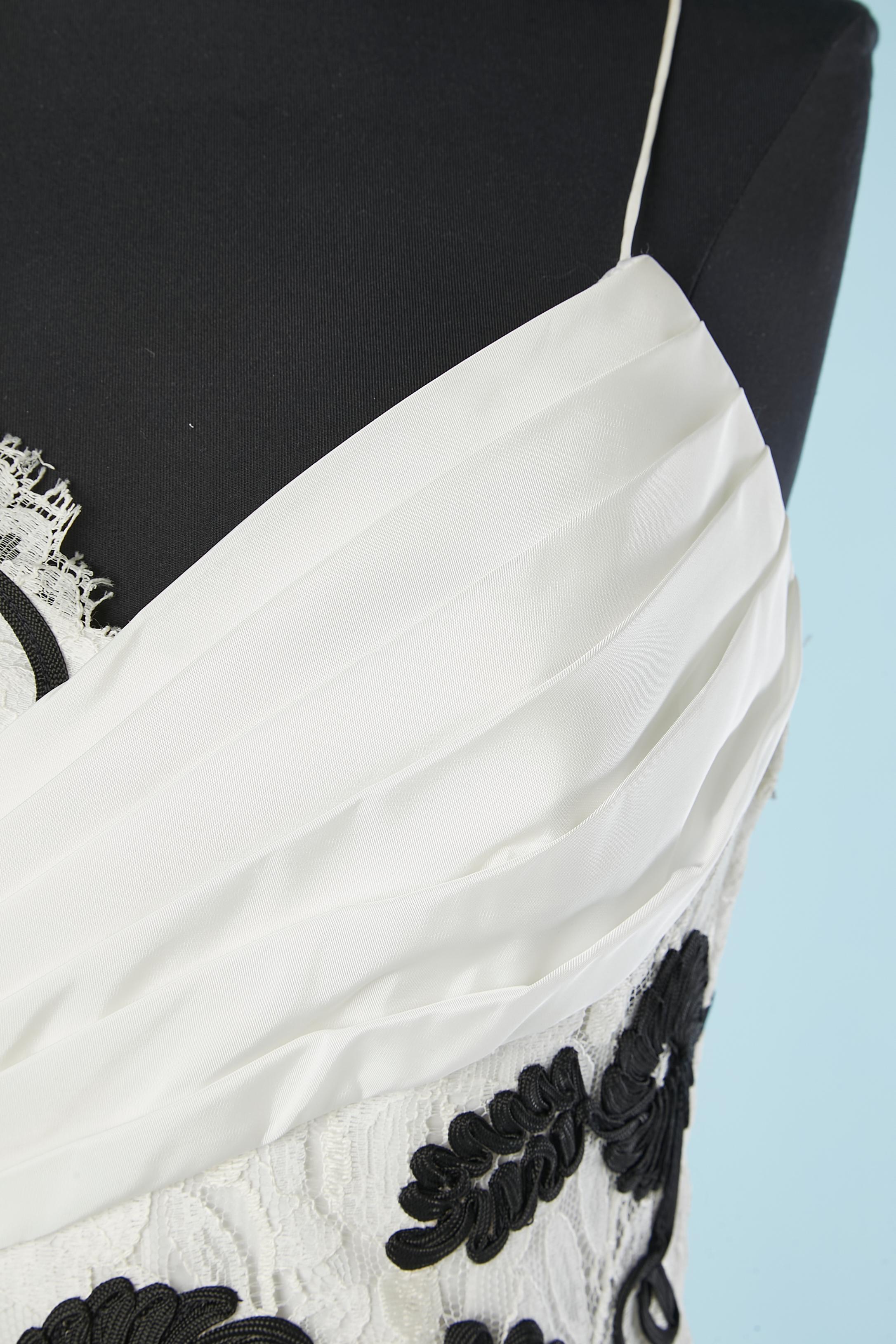Robe de cocktail en dentelle blanche avec application de fleurs noires . Hanches et encolure drapées  avec nœud surdimensionné sur le côté des hanches (composition du tissu : nylon et polyester) Le nœud est maintenu par un bouton-pression et un