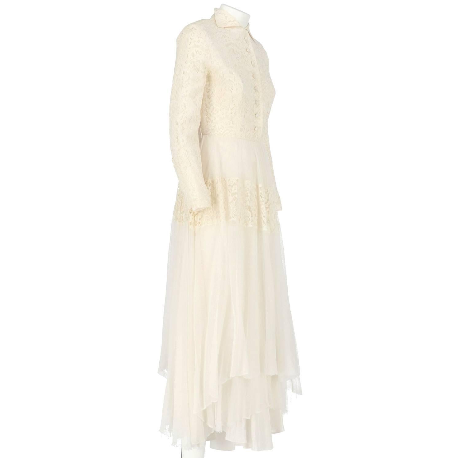 Precioso vestido de novia blanco roto con encaje y velo de tul. Tiene manga larga, falda recta, hombros acolchados, cierre con botones de presión en la parte delantera y cuello con dos pequeños reversos, y cierre lateral con cremallera. El artículo