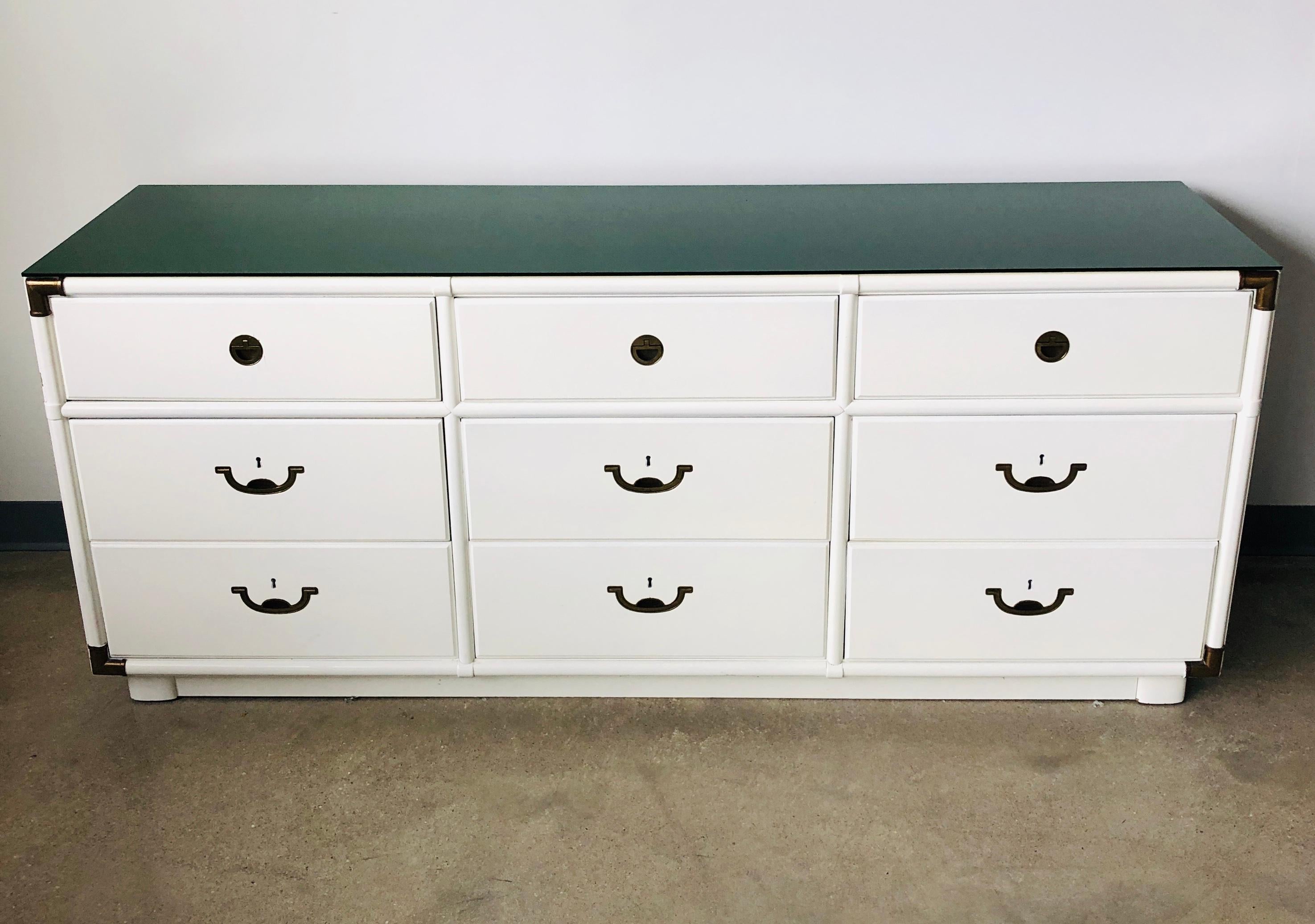 Offered is a Mid-Century Modern signed Drexel lacquered in white campaign dresser with brass hardware and a removable emerald green Lucite top. We love vintage 1970s campaign furniture! This fabulous dresser is lacquered in bright white with