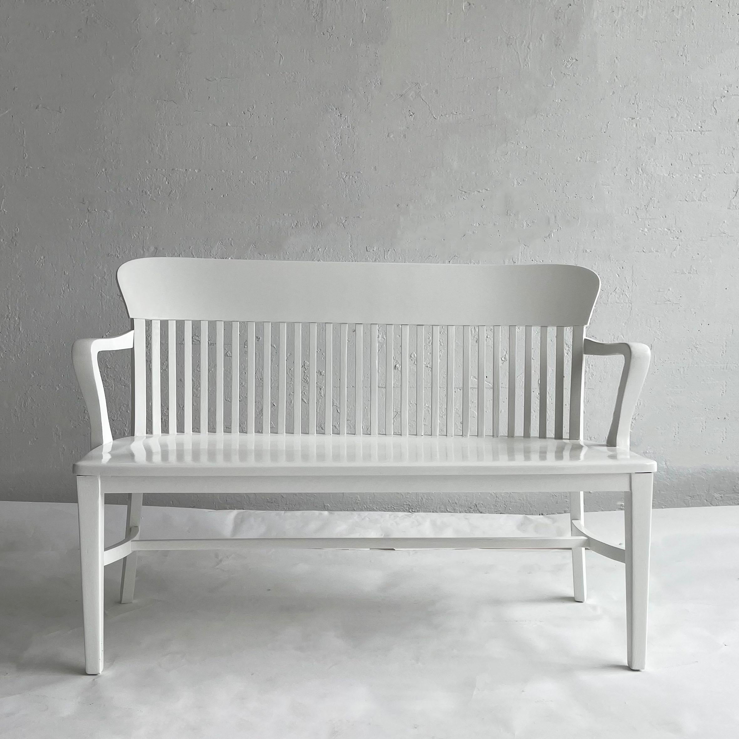 Classic, industrial, midcentury, bank of England or court bench lacquered in crisp satin white features a contoured seat and slat back. This iconic piece works with any decor and numerous uses from an entryway bench to dining room seating.