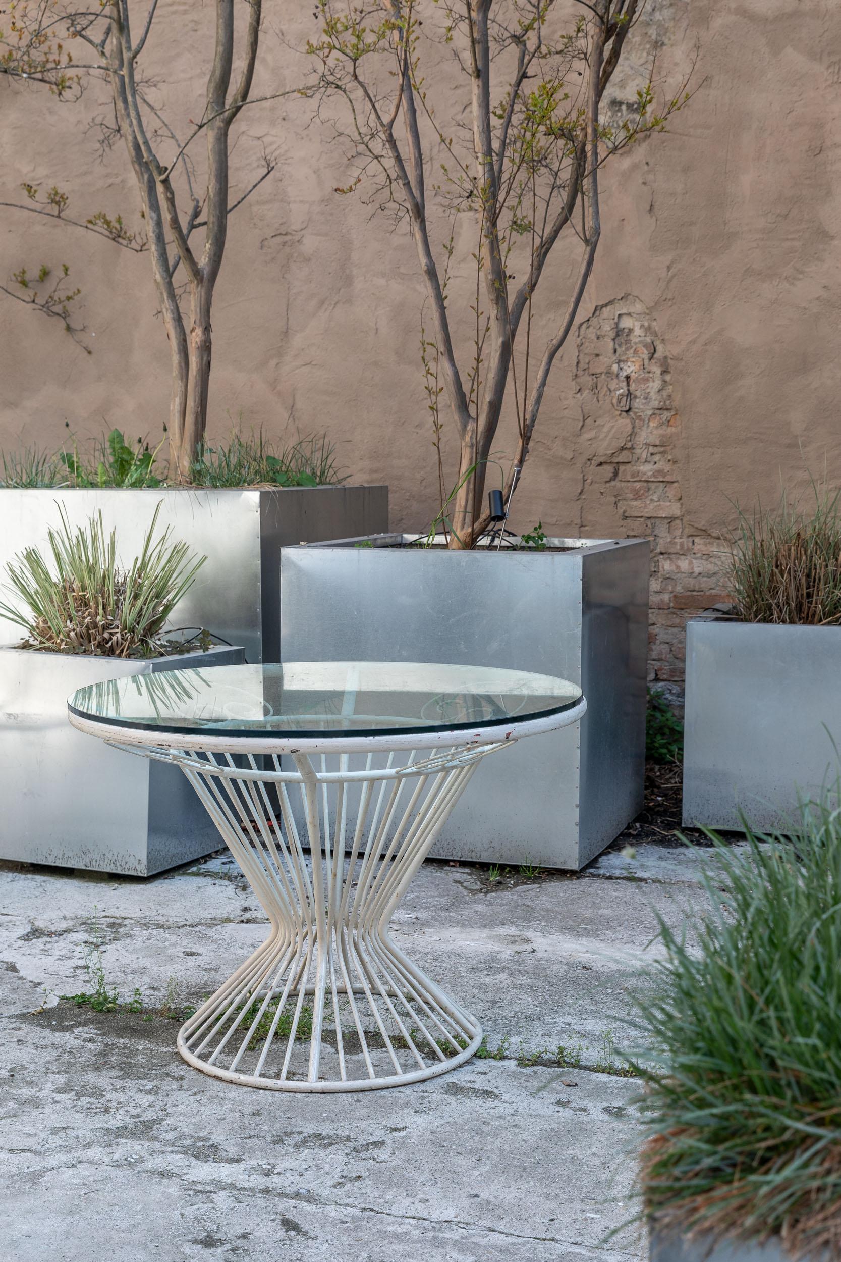 Outdoor white lacquered iron round table. The peculiar radiate shape of the base holds a really thick clear glass top. The table is in the style of Gio Ponti.
