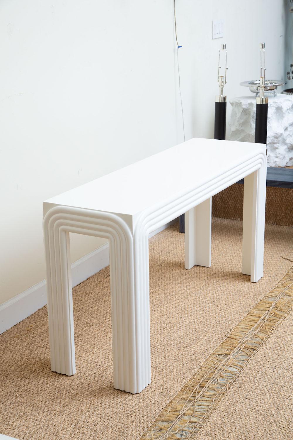 This newly restored vintage white lacquered over wood console table or sofa table has 4 curved banded applied raised designs. It has been restored to the best it can be now. The top is not completely smooth; as is commensurate with age. This is very