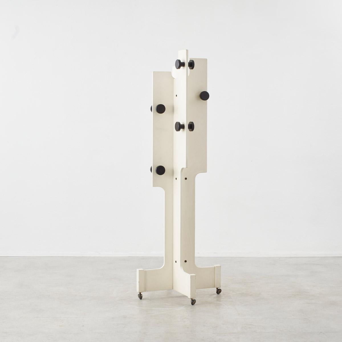 Playfully reflecting the silhouettes of the Memphis movement, this white lacquered wooden coat stand is formed of sharp lines and strong curves complimented by bold black knobs dotted across the structure. The stand is on four wheels, allowing for