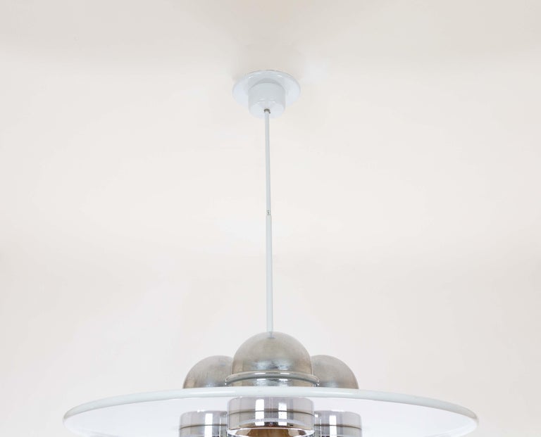Large Lampros pendant designed by Ettore Sottsass Jr. and produced by Stilnovo in the 1970s.

This disc-shaped model consists of a white aluminium shade and three chromed metal reflectors. It has the manufacturer's mark engraved at the top of the