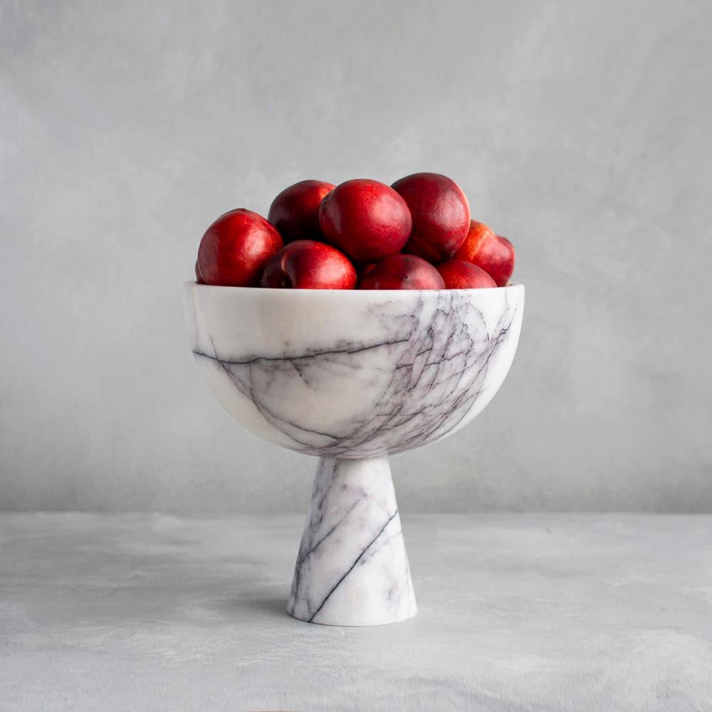 A substantial white marble bowl with unique lilac veining rests atop a pedestal for a grand presentation of fruits and vegetables. 

Exposure to the acid of citrus fruits can stain marble. Due to the natural properties of marble the colour and