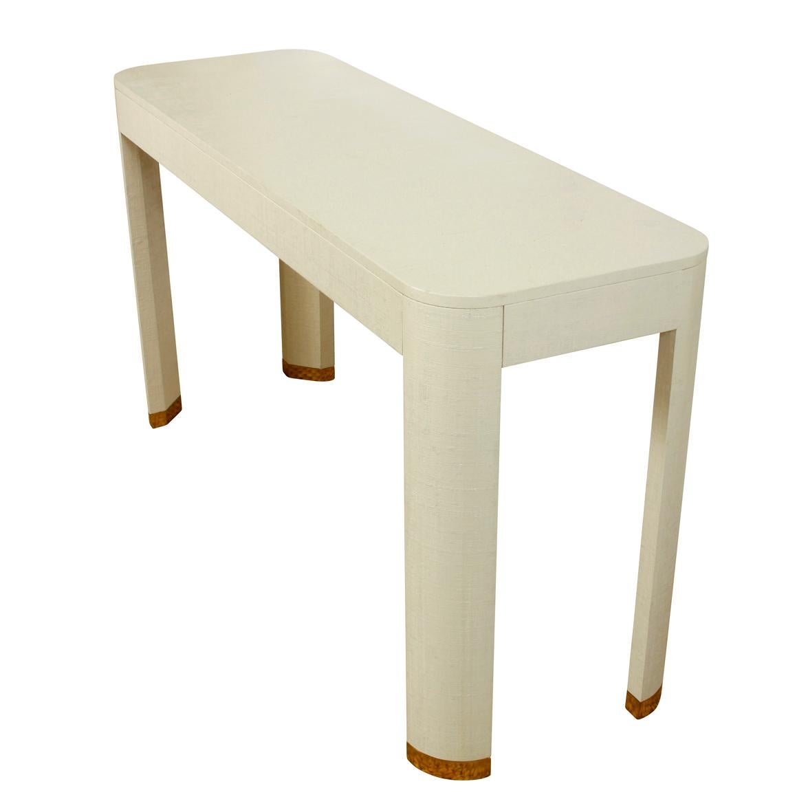 White linen wrapped console table with brass feet and curved edges.