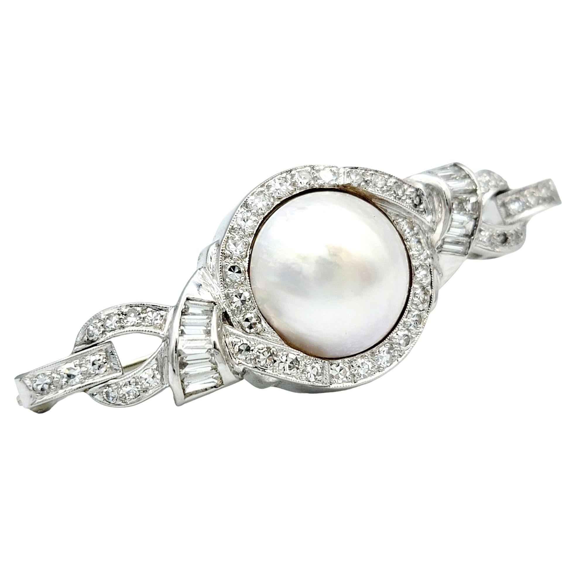 This exquisite brooch will bring elegance and artistry to your fine jewelry collection. At its heart, a resplendent mabe pearl, an iridescent and lustrous marvel, commands attention with its timeless allure. It is cradled within an intricate ribbon