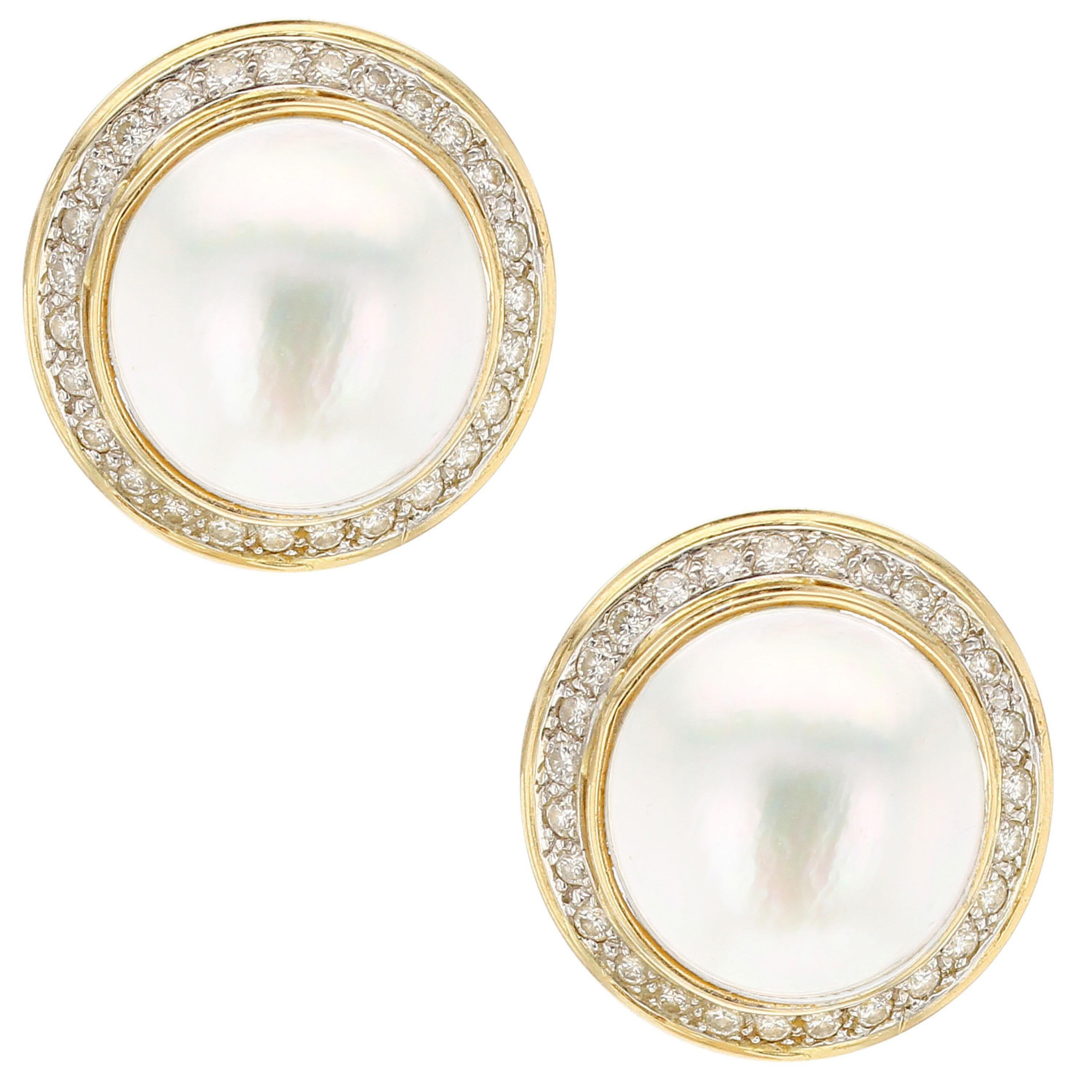 A 16.40 MM White Mabe Pearl Pair of Earrings, each wrapped with a circle of 26 round brilliant-cut diamonds in 14K Yellow Gold. Pierced clip backs. Earring Length: 0.80”