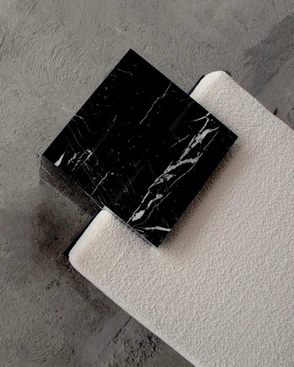 The coexist bench uses balance and delicate harmony of materials meeting. The bench consists of a black steel frame, Nero Marquina marble cubes, and mattress upholstered in bouclé fabric. 

The pieces fit together seamlessly, with the marble cubes