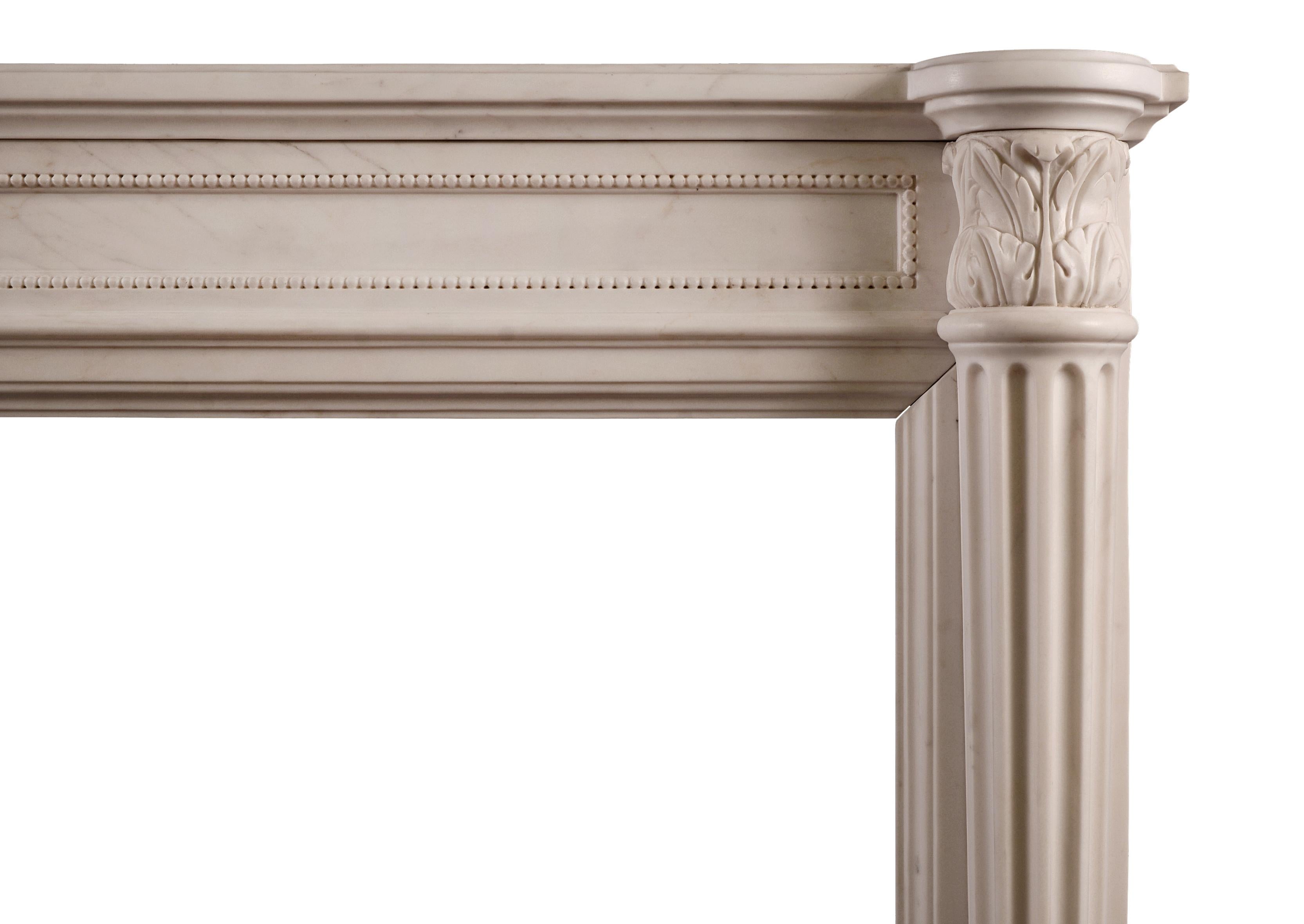 Une élégante cheminée française de style Louis XVI en marbre blanc, avec une frise lambrissée et perlée, des colonnes cannelées demi-rondes effilées avec des chapiteaux sculptés de feuilles d'acanthe. Une copie d'une pièce antérieure.

N.B. Peut