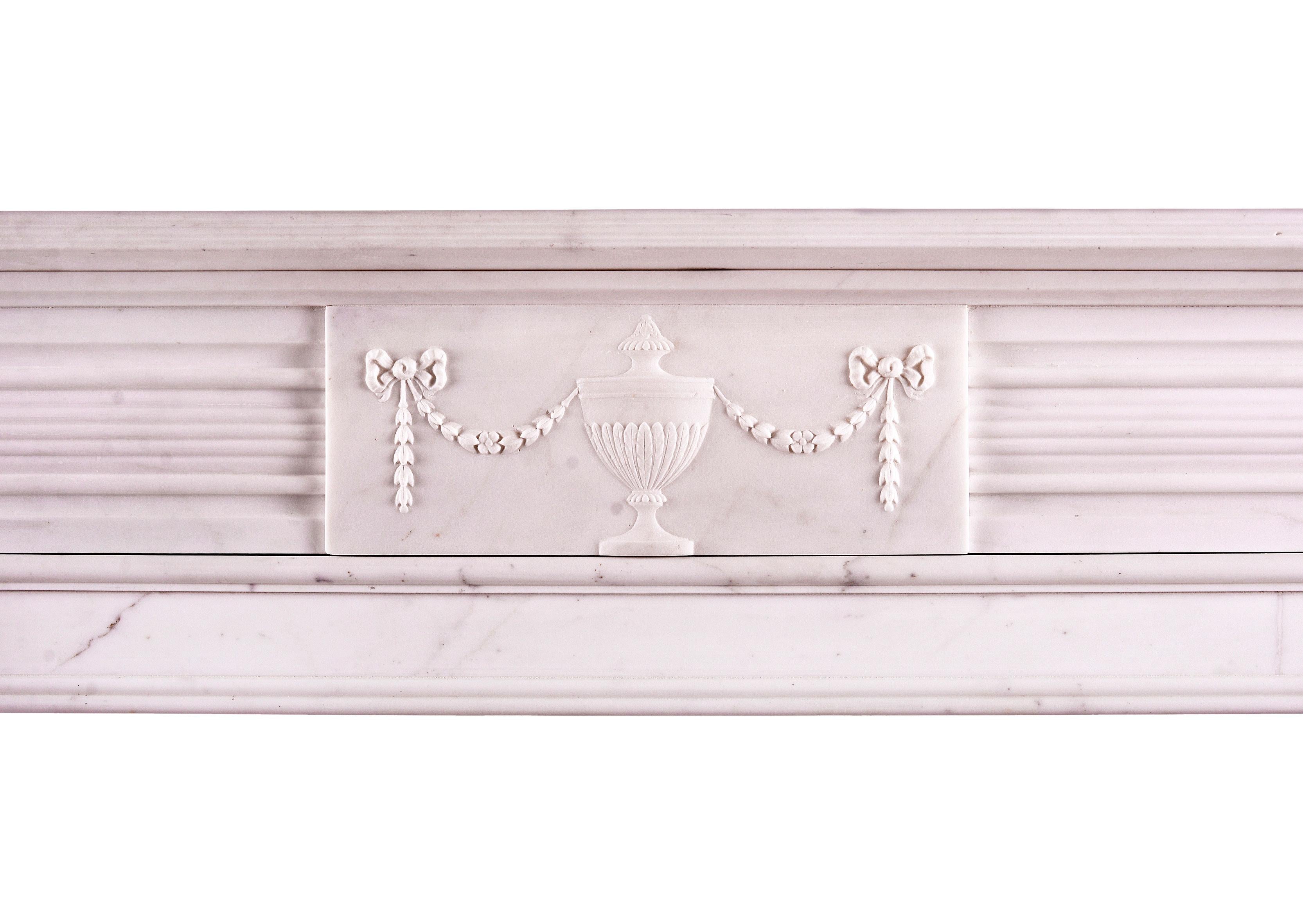 A white marble fireplace in the Regency style. The fluted jambs surmounted by finely carved paterae, the frieze with centre block featuring swags, flowers and classical urn. Reeded shelf above. English, circa 1900.

Shelf Width	        1464 mm    57