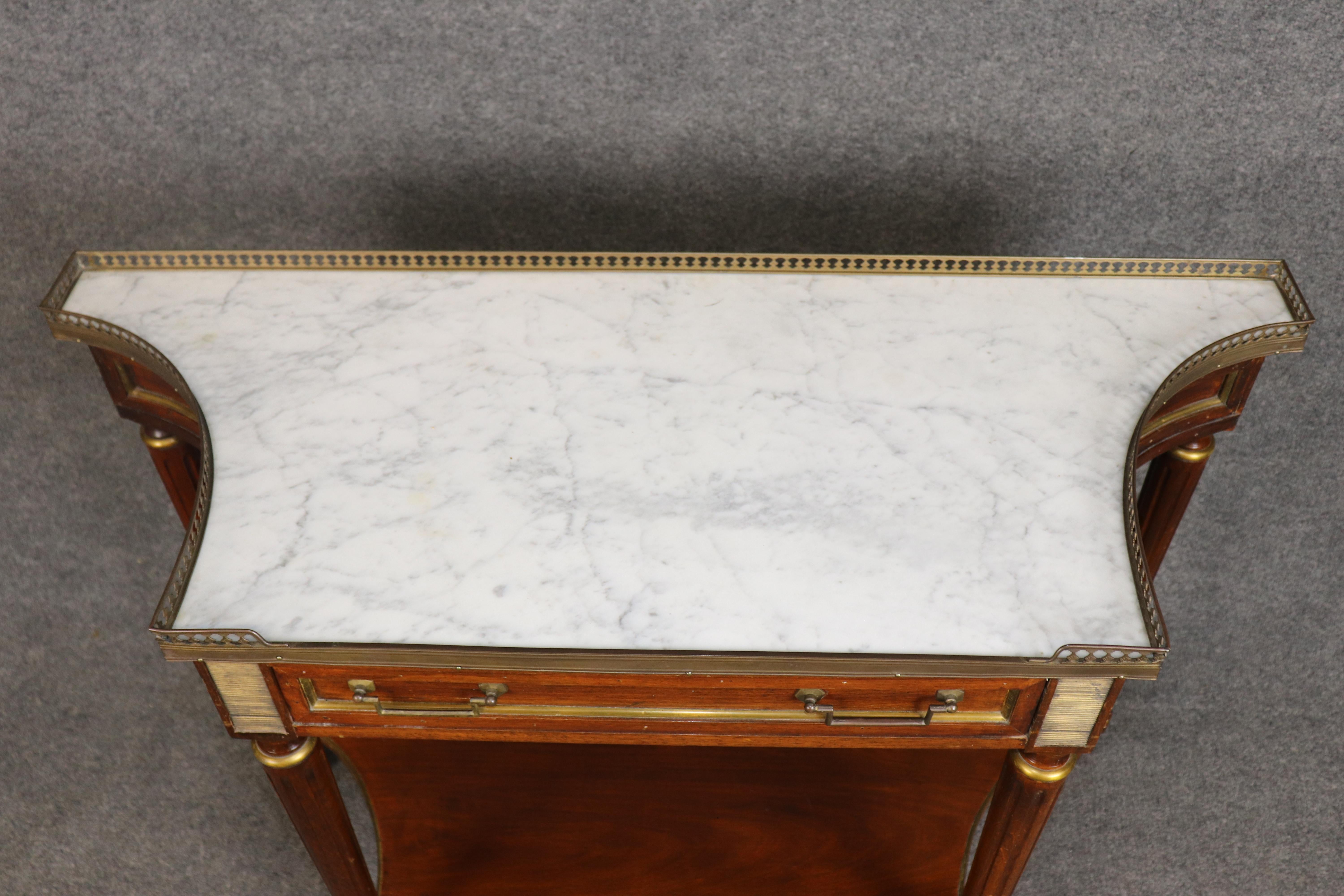 Esta exquisita consola de estilo Directoire francés, fabricada en Italia e inspirada en la Maison Jansen, irradia una refinada elegancia neoclásica. La mesa presenta un hermoso tablero de mármol blanco rodeado por una intrincada galería de latón,