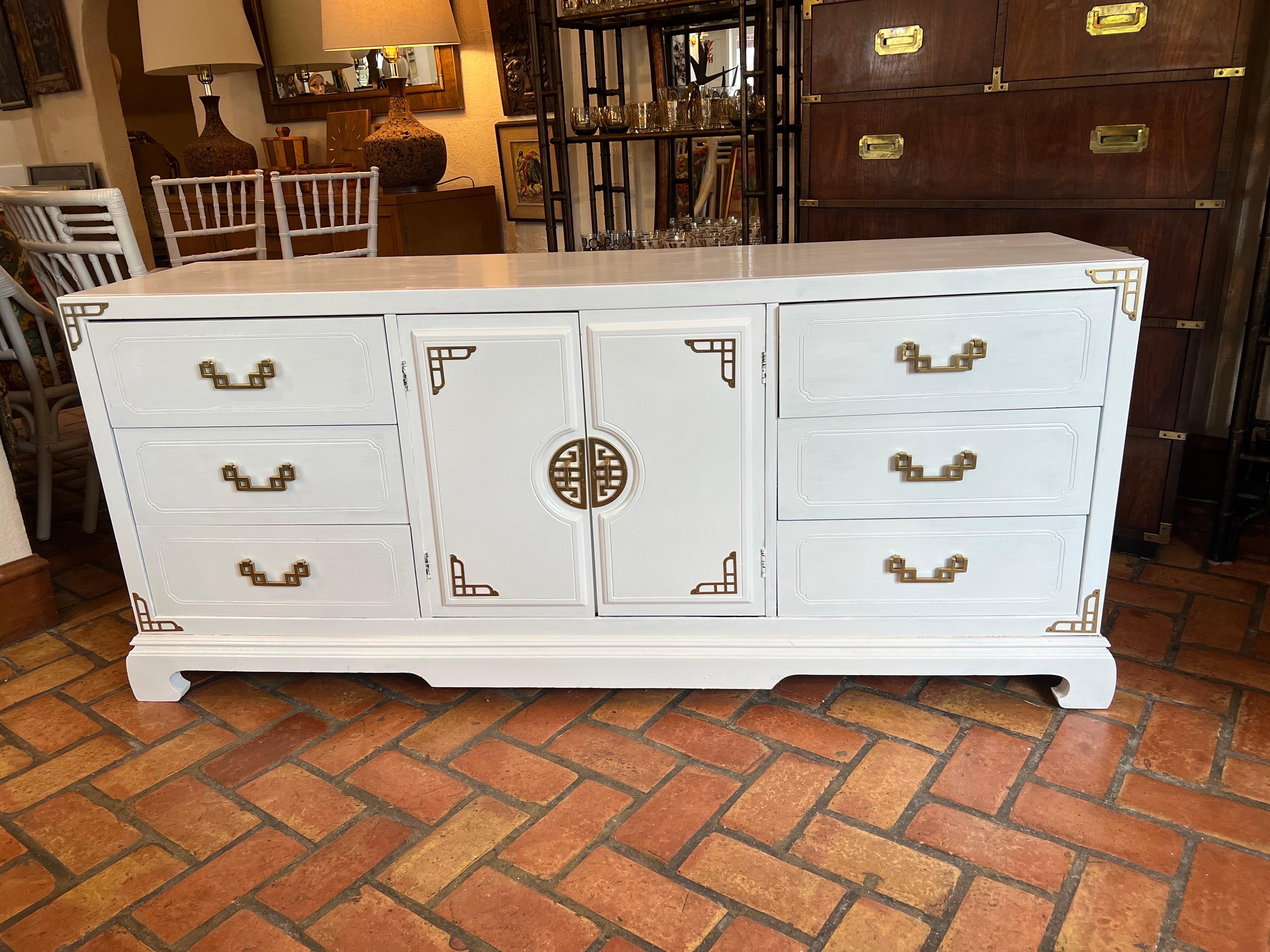 Mid-Century Modern white dresser or credenza by Bassett. Asian styling with curved Ming legs in front. In the style of Ray Sabota with its chunky brass hardware and Greek Key design. 
A statement piece for that bedroom or living space. Center