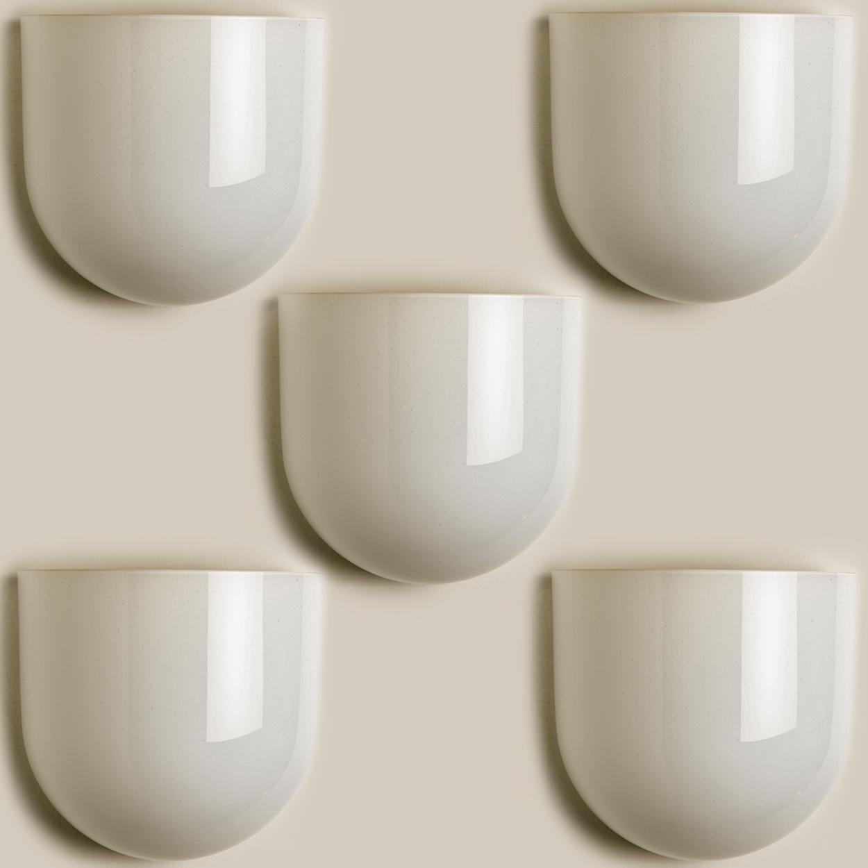 Beautiful white milkglass wall lights with small air bubbles. The lights are half cylinder shaped.
They are manufactured by the company Glasshütte Limburg, in Germany, Europe around 1970.

This wall light gives a warm light that suits any
