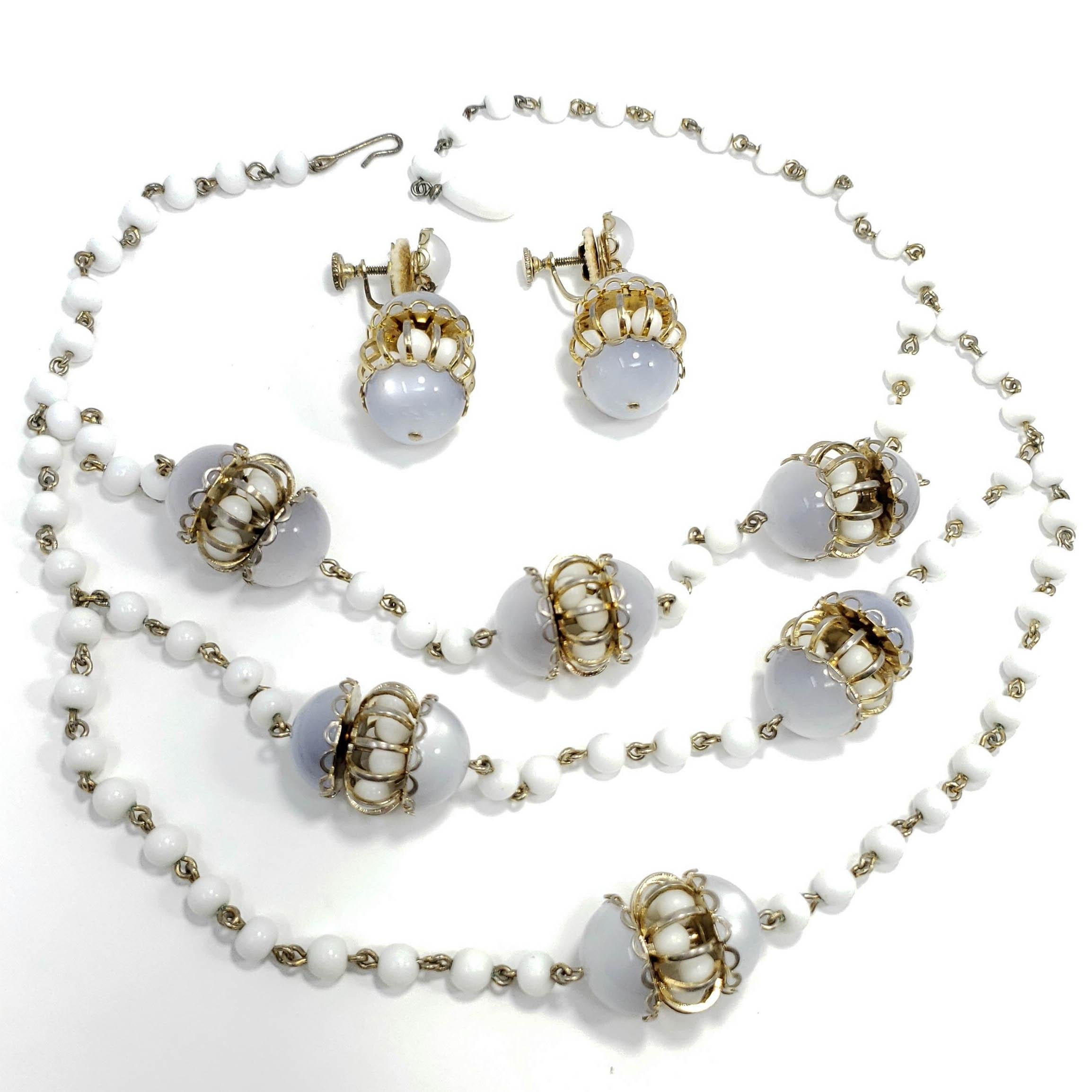 Matching moonglow lucite and milk glass bead multi-strand necklace and earring set. The necklace features decorative lucite and milk glass chamber charms set on a multi-strand milk glass bead necklace. Each earring features a matching charm, set on