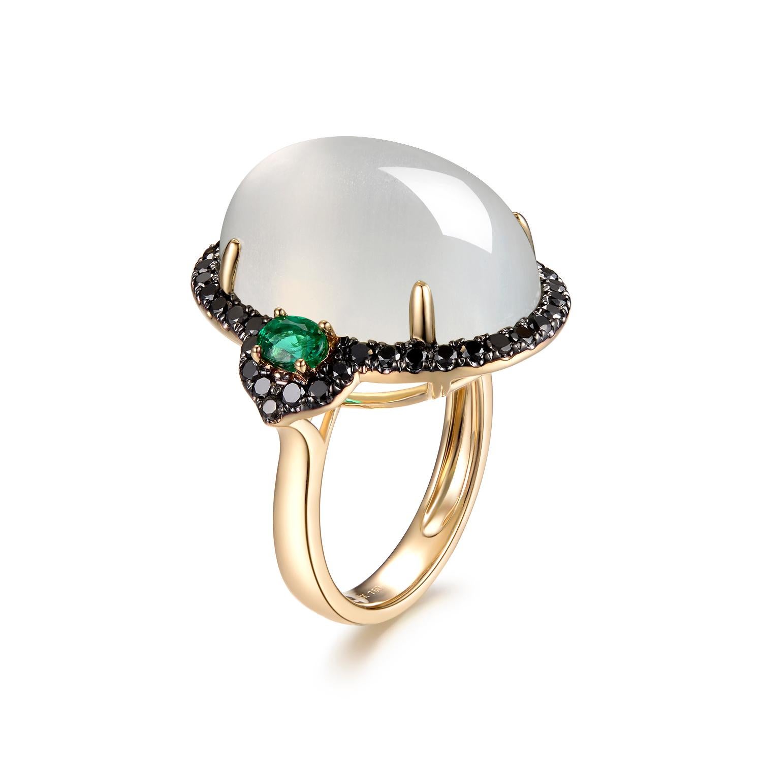 This pretty ring features a large oval moonstone weighing 24.39 carats with beautiful adularescence. . This moonstone is an impressive size, set in a dazzling black diamonds halo flanked with 2 emeralds 14k yellow gold design that showcases its