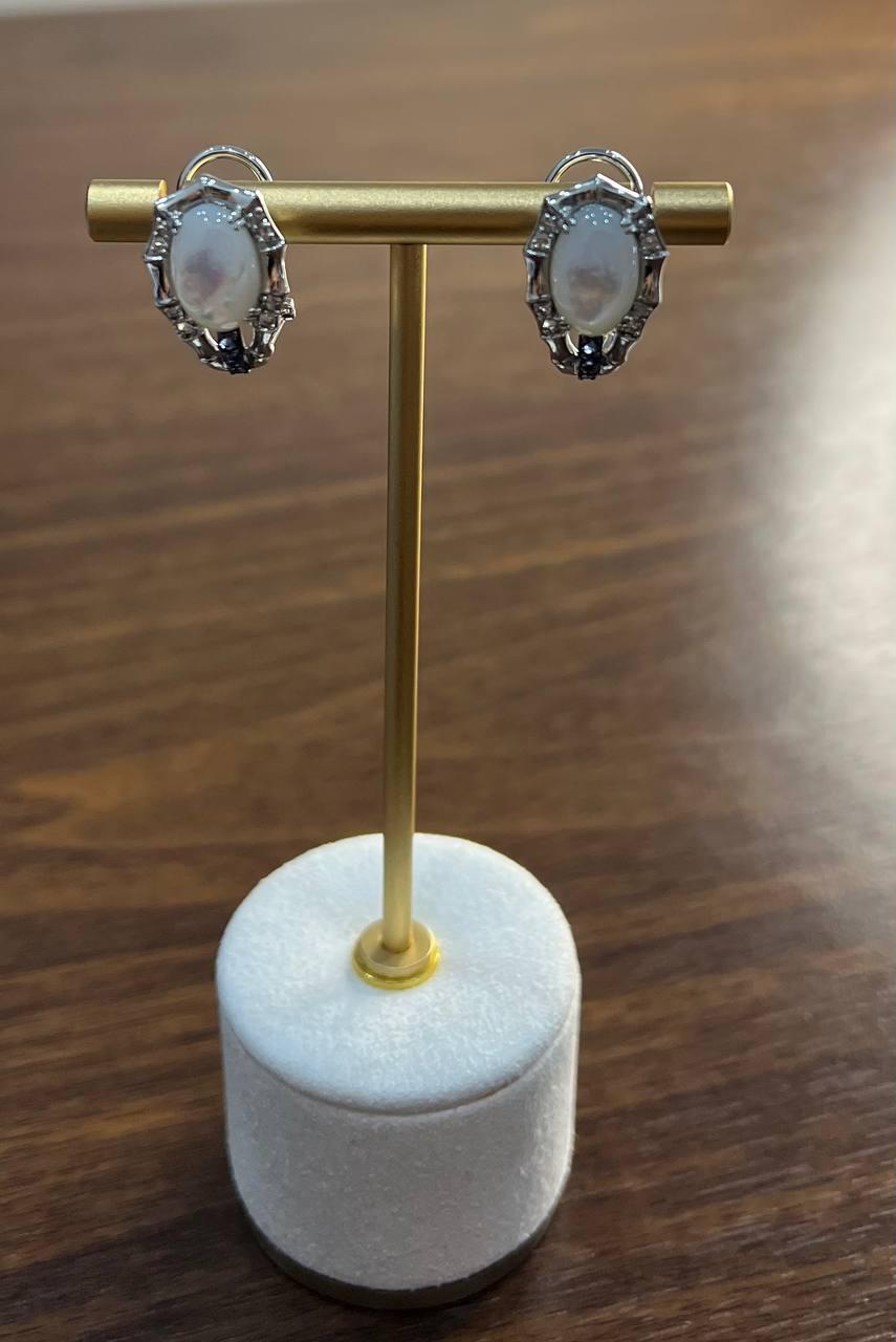 Elaborados en oro blanco de 14 quilates, estos pendientes llevan madreperla blanca de talla ovalada. Las piedras blancas están engarzadas en un intrincado diseño, mostrando su belleza natural.