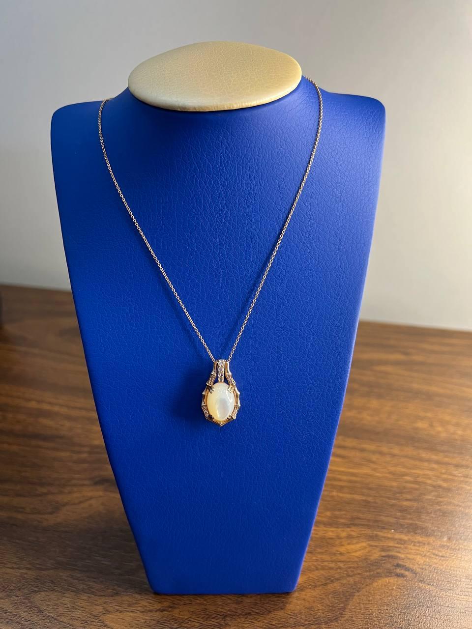 A refined pendant necklace featuring an oval white mother of pearl centerpiece, encircled by a delicate arrangement of small, sparkling diamonds. The opal is set in a gold frame with a bamboo-like design, enhancing its natural beauty. The pendant is