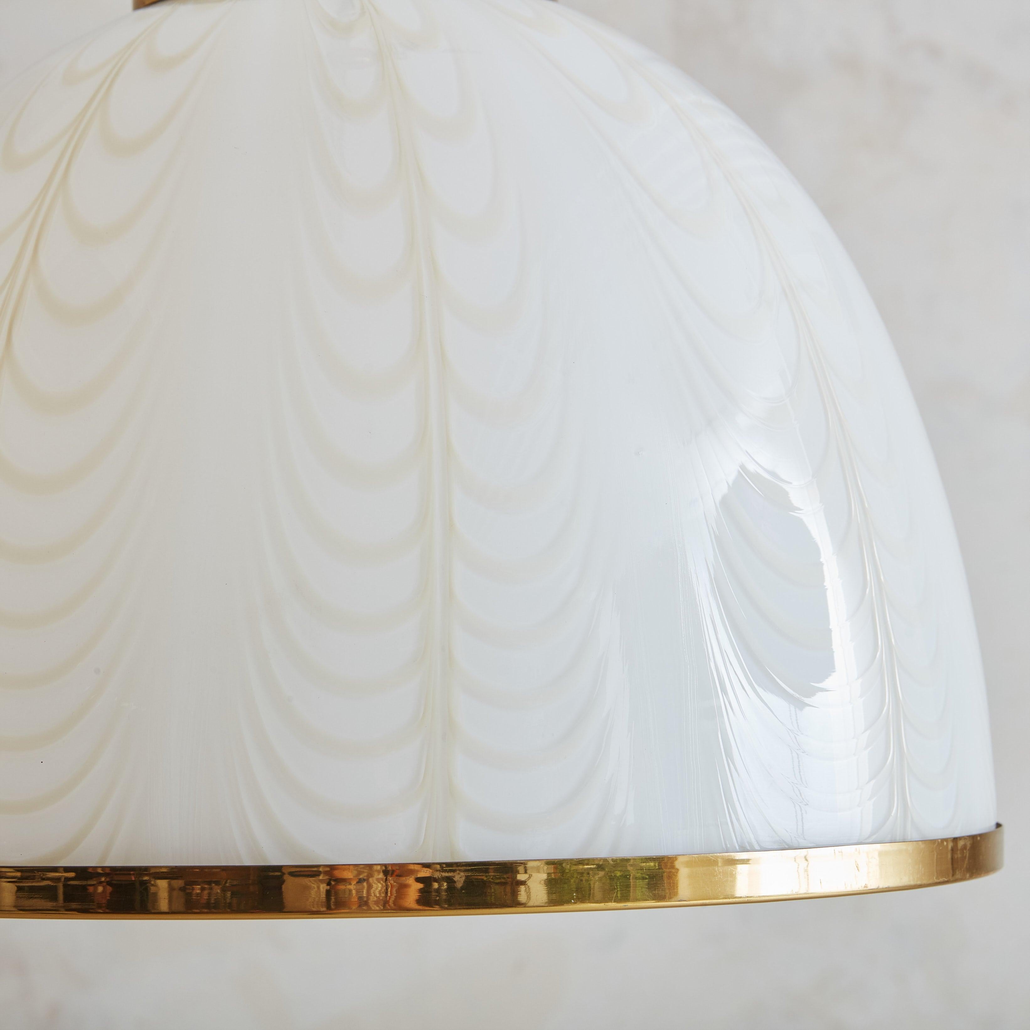 A 1970s Italian pendant light designed by F. Fabbian for Mazzega. This pendant features a white Murano glass dome shade with a stunning etched ripple design in a subtle beige hue. The shade is elegantly accented with a brass rim and hangs from a