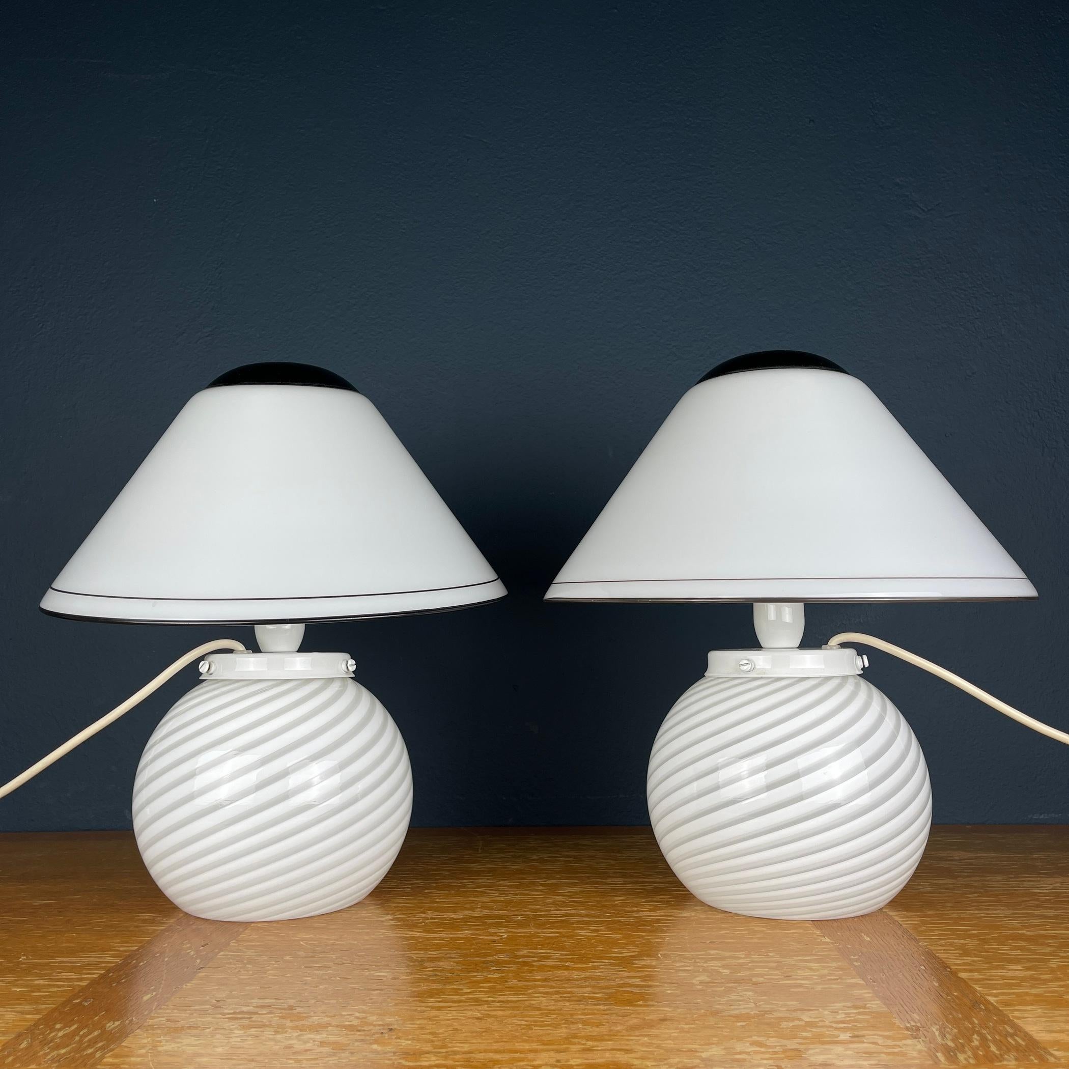 Sehen Sie sich dieses exquisite Paar Murano-Pilzlampen an, die in den lebhaften 1970er Jahren in Italien mit Präzision gefertigt wurden. Jede Leuchte ist ein Zeugnis der zeitlosen Anziehungskraft von gewirbeltem Glas, das bezaubernde Muster in Ihren