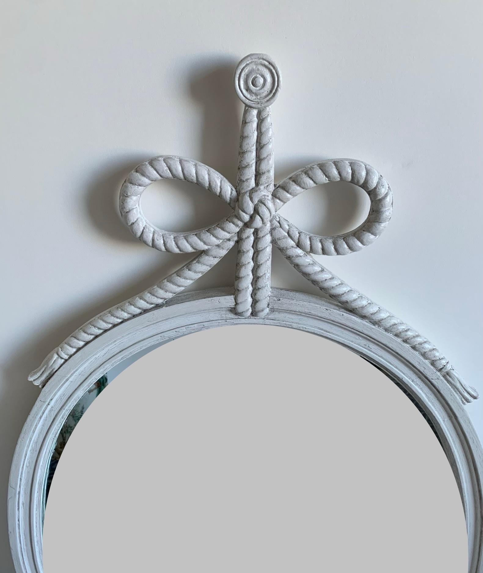 White neoclassical style oval mirror. Original mirrored glass with overall antiquing. Carved rope and bow detailing. Newly refinished in an antique white painted finish.
