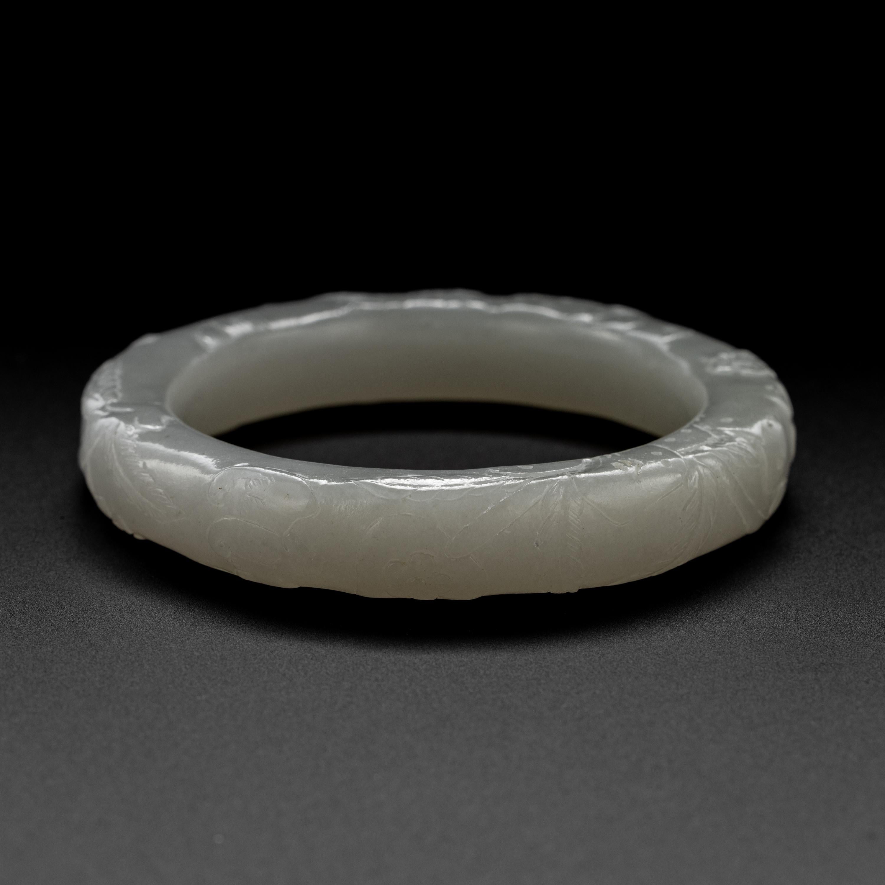 This 60mm hand-carved white nephrite jade bangle is exceptionally beautiful and rare. It has exquisite proportions, being thicker than many bangles. It has been etched and carved to depict blossoms, feathers, and several soaring phoenixes.  This is