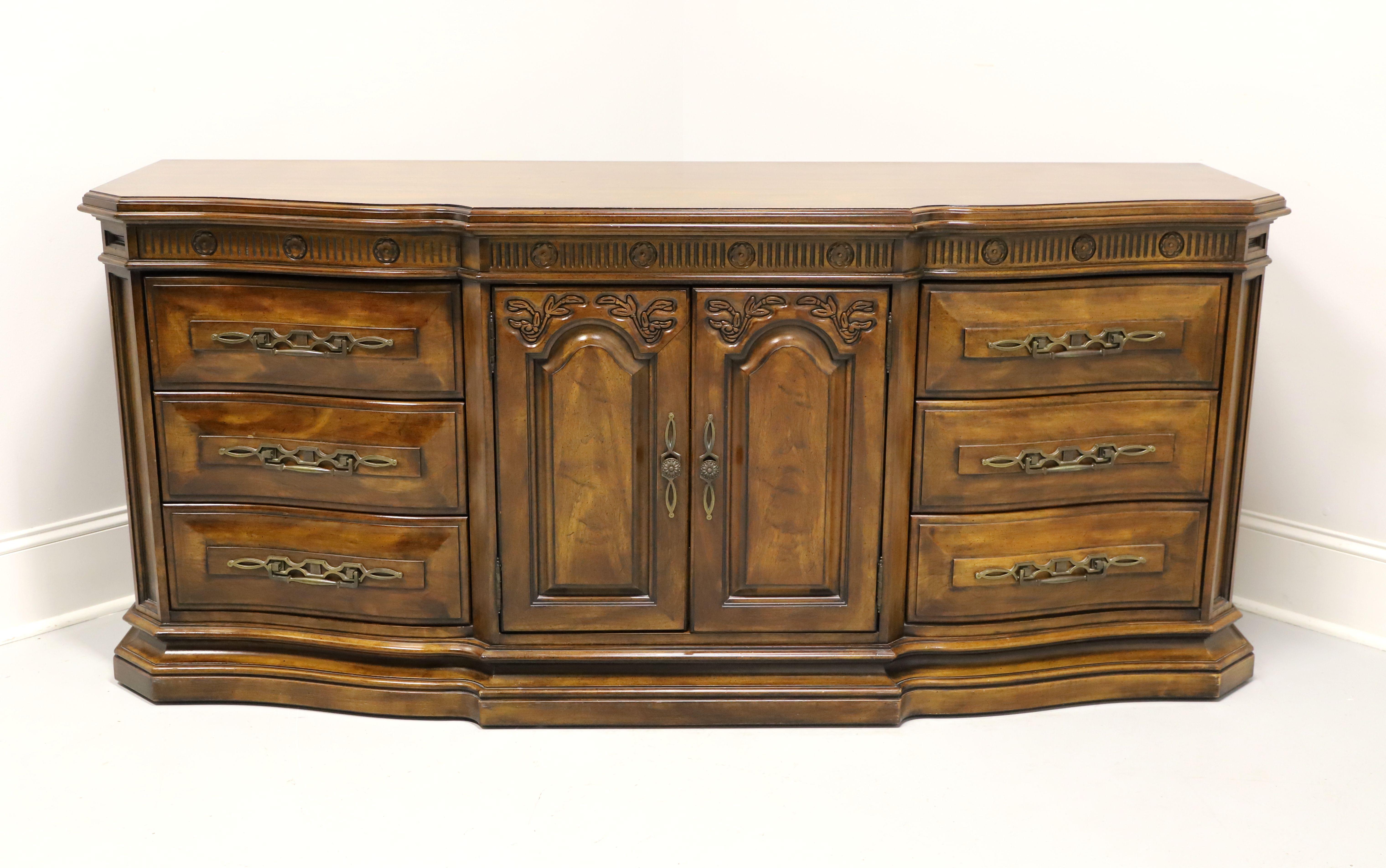 A French Country style triple dresser by White Furniture. Solid cherry wood with slightly distressed finish, ogee edge to the top, serpentine shape, brass hardware, decoratively carved frieze over doors & drawers, raised door & drawer fronts, and a