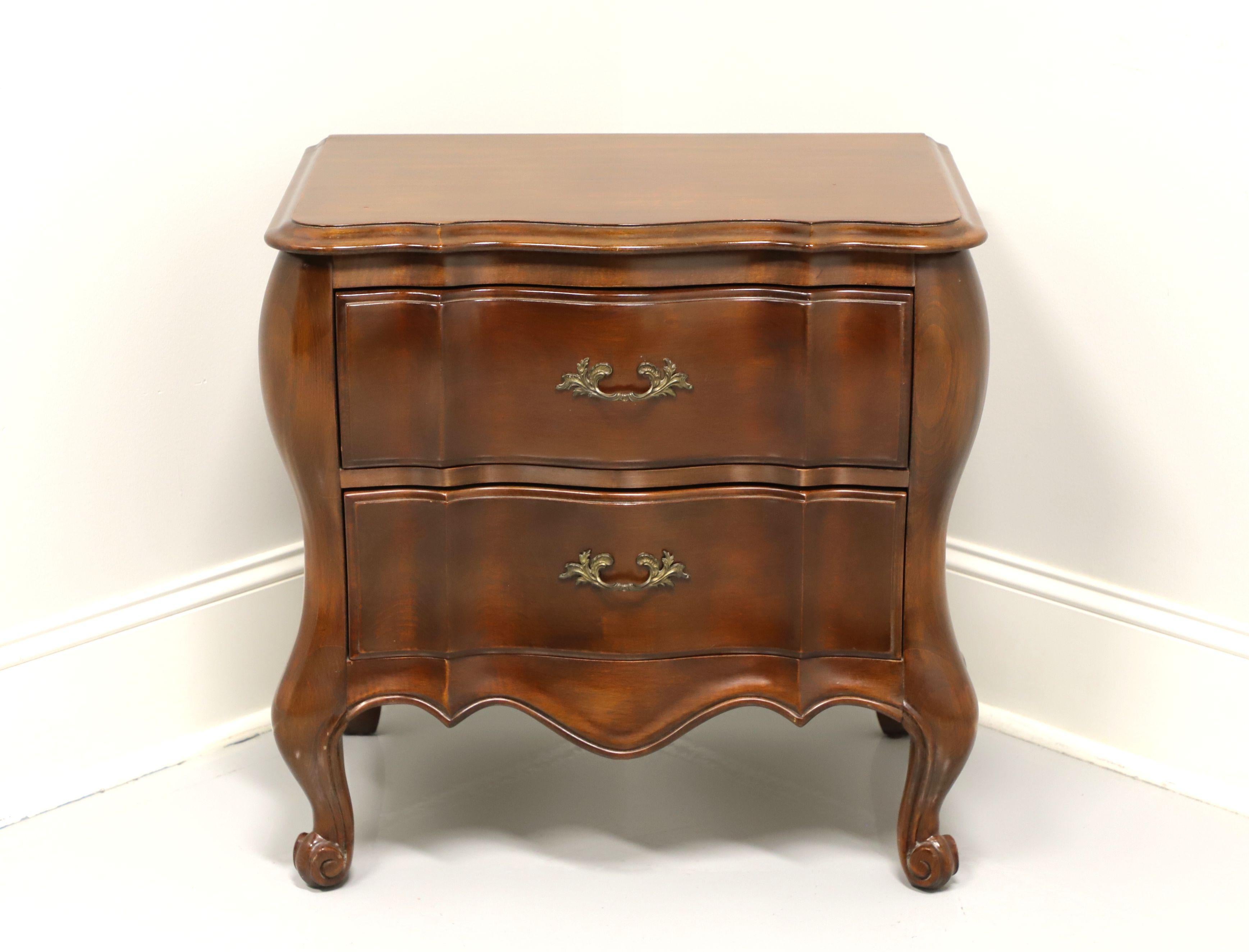 A French Country style nightstand by White Furniture, of Mebane, North Carolina, USA. Walnut with brass hardware, curved front, carved apron and scroll front feet. Features two drawers of dovetail construction. Made in the late 20th