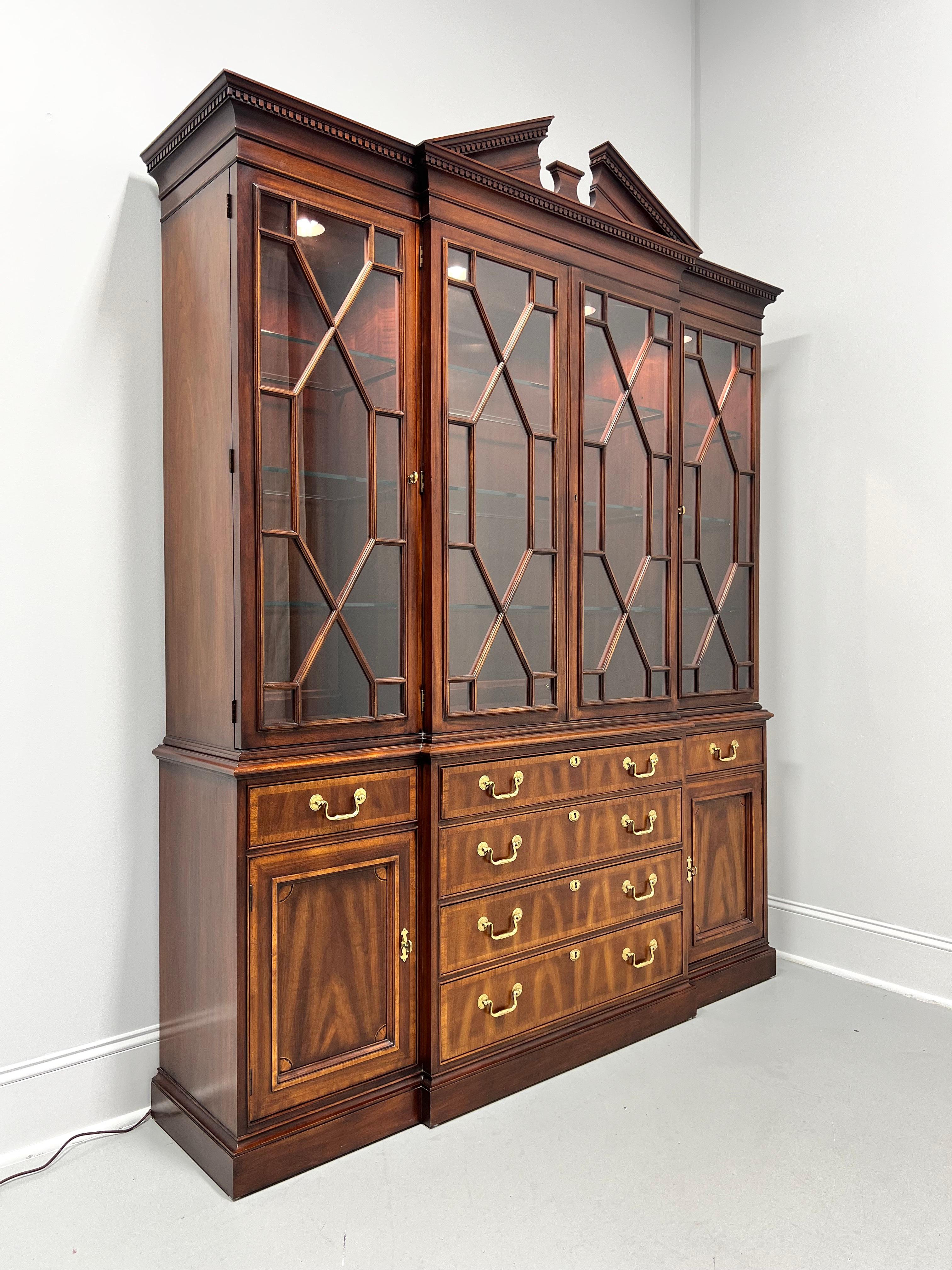A Chippendale style breakfront china cabinet by White Furniture. Mahogany with inlays, banded door & drawer fronts, brass hardware, pediment to the top with crown & dentil molding, glass doors with fretwork panes, ogee edge to top of lower cabinet,