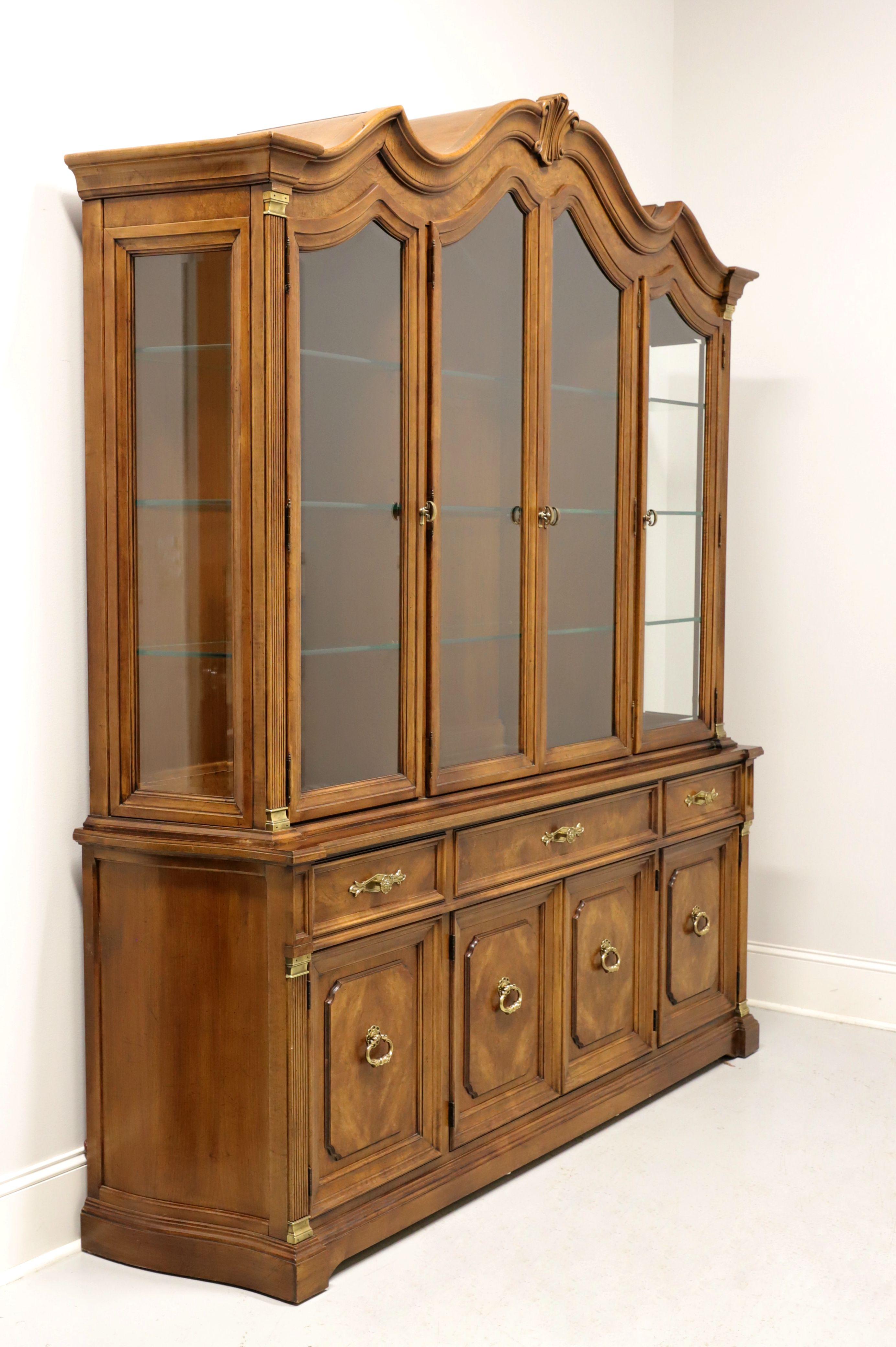 A monumental china cabinet in the French Provincial style by White Furniture, of Mebane, North Carolina, USA. Walnut and burl walnut with brass hardware, arched top and fluted side columns. Lighted upper cabinet has four arched beveled glass doors,