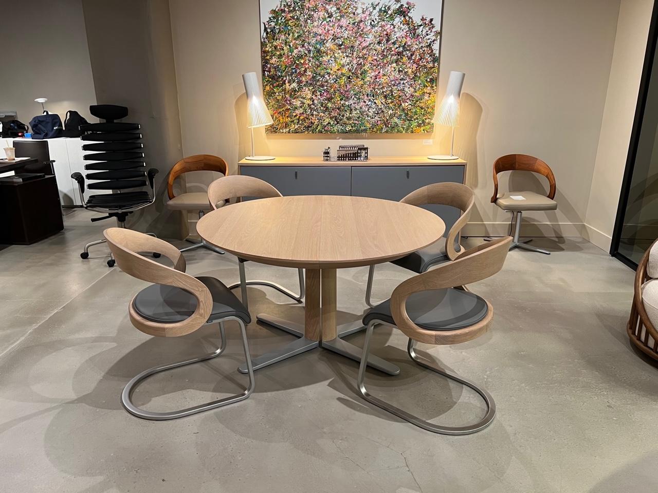 Girado Extending table in white oiled oak and matte grey glass insert. 
Feet in matte aluminum. 

The table closed is a round and opens into an oval.  The self storing leaf features a soft closing butterfly mechanism. 

Dimensions:
51