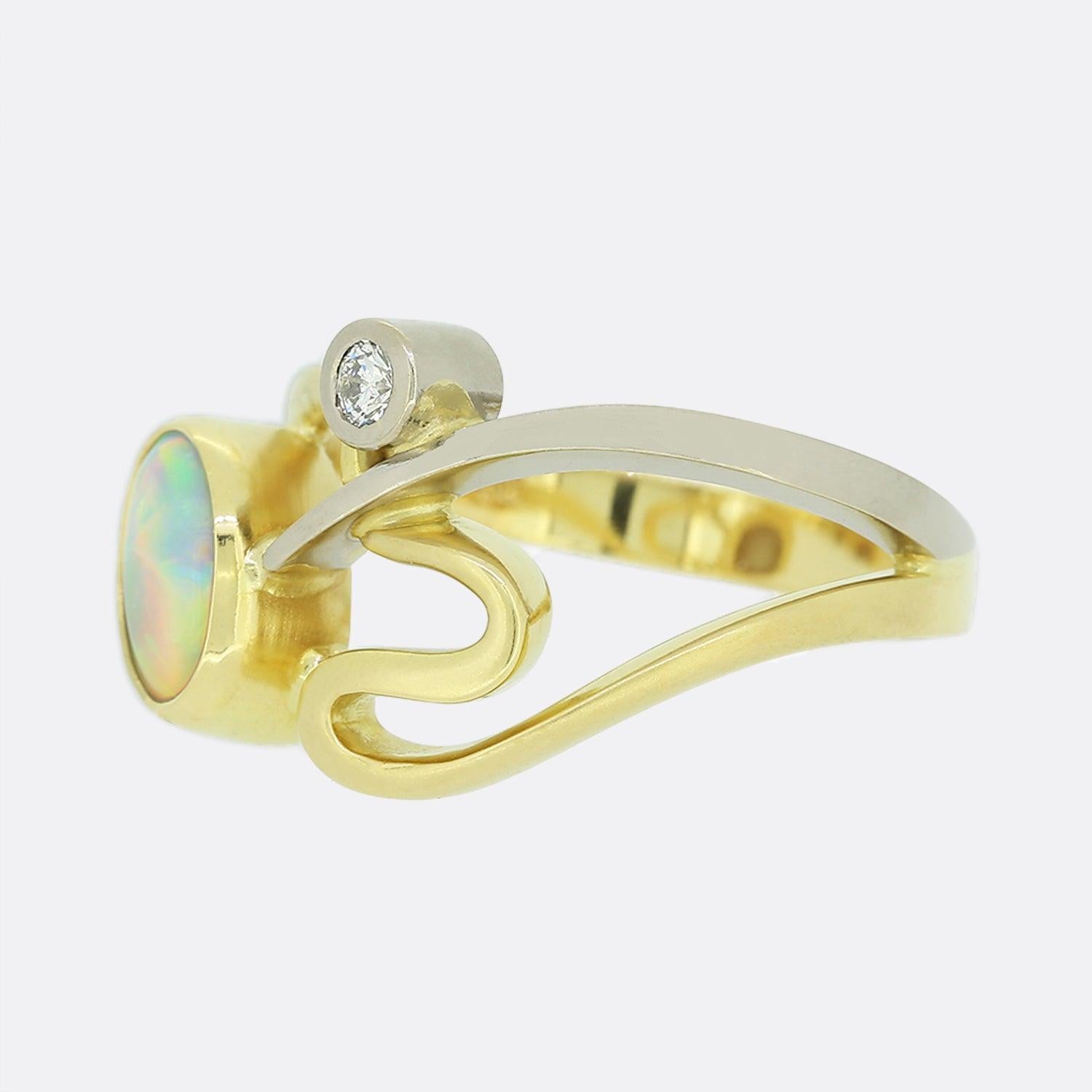 Here we have an 18ct yellow gold white opal and diamond abstract ring. The focal opal here is bezel set, oval cut and has a wondrous play of colour. This main stone is complemented by a single round cut natural diamond which sits just below upon a
