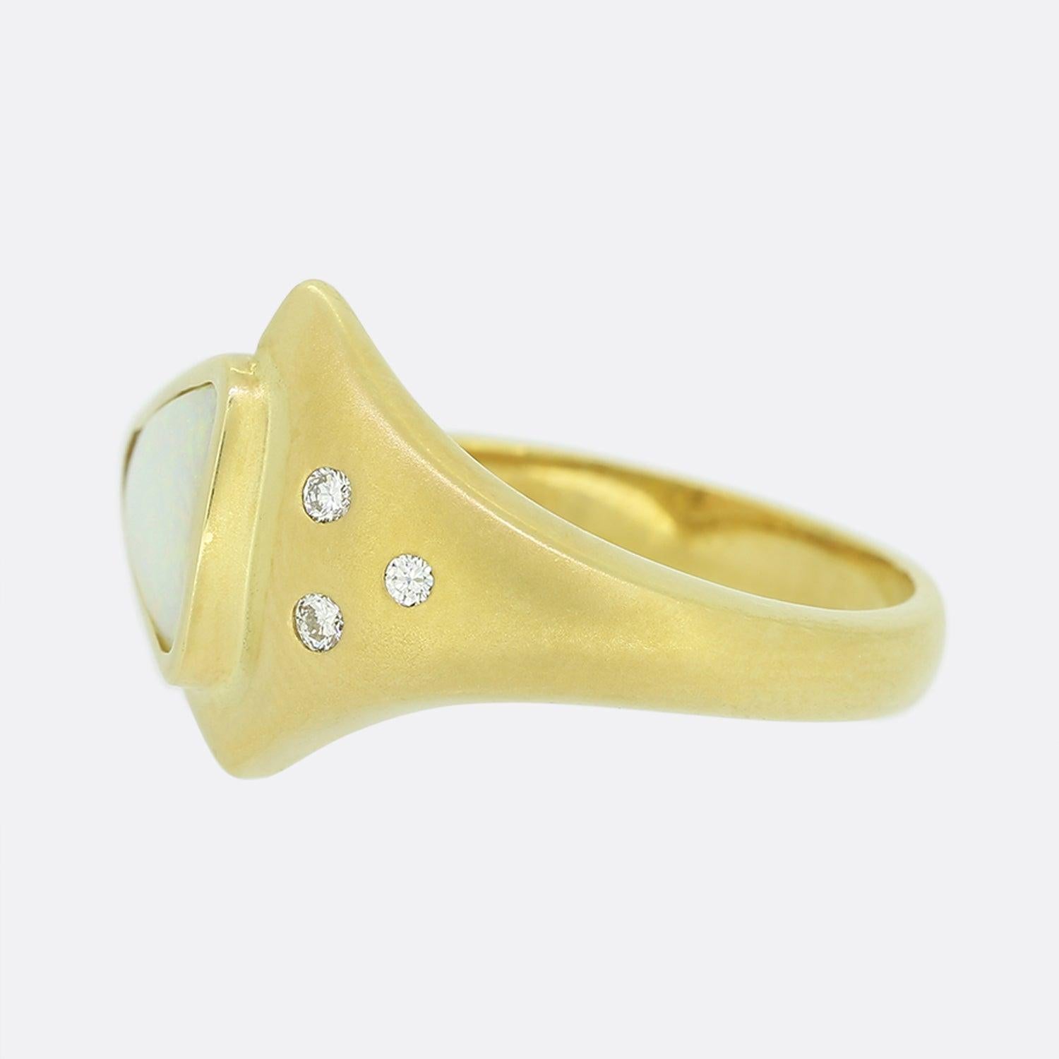 This is an 18ct yellow gold white opal and diamond abstract ring. The central opal is rub-over set, triangular shaped and has an excellent white body of colour. This focal stone plays host to a trio of round cut natural diamonds; all of which sit