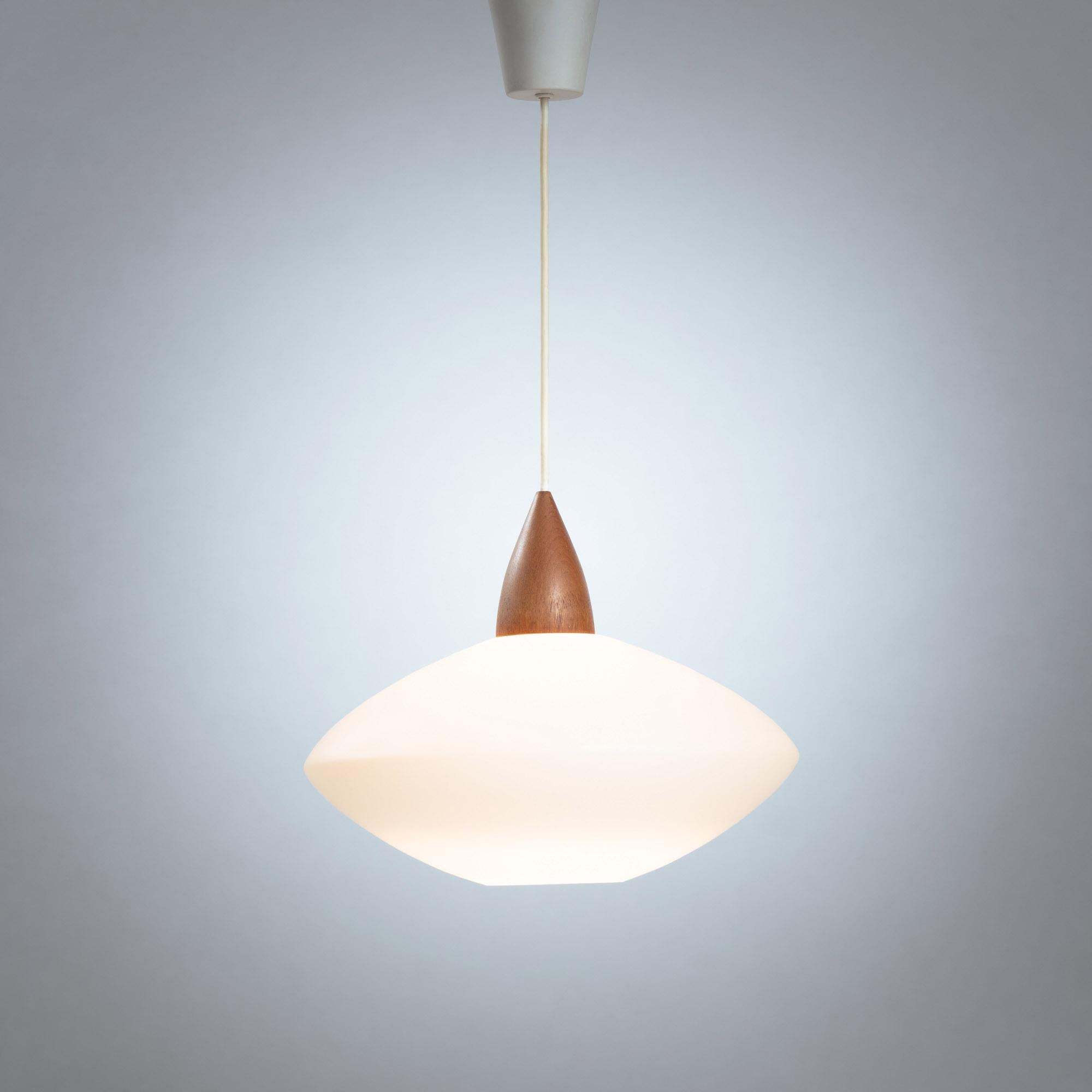 This beautiful ufo pendant light in opaline glass with teak in great condition was designed and produced by Swedish designers and brothers Uno & Östen Kristiansson in the 1950s
They where known for their lighting and mirror designs, and particularly