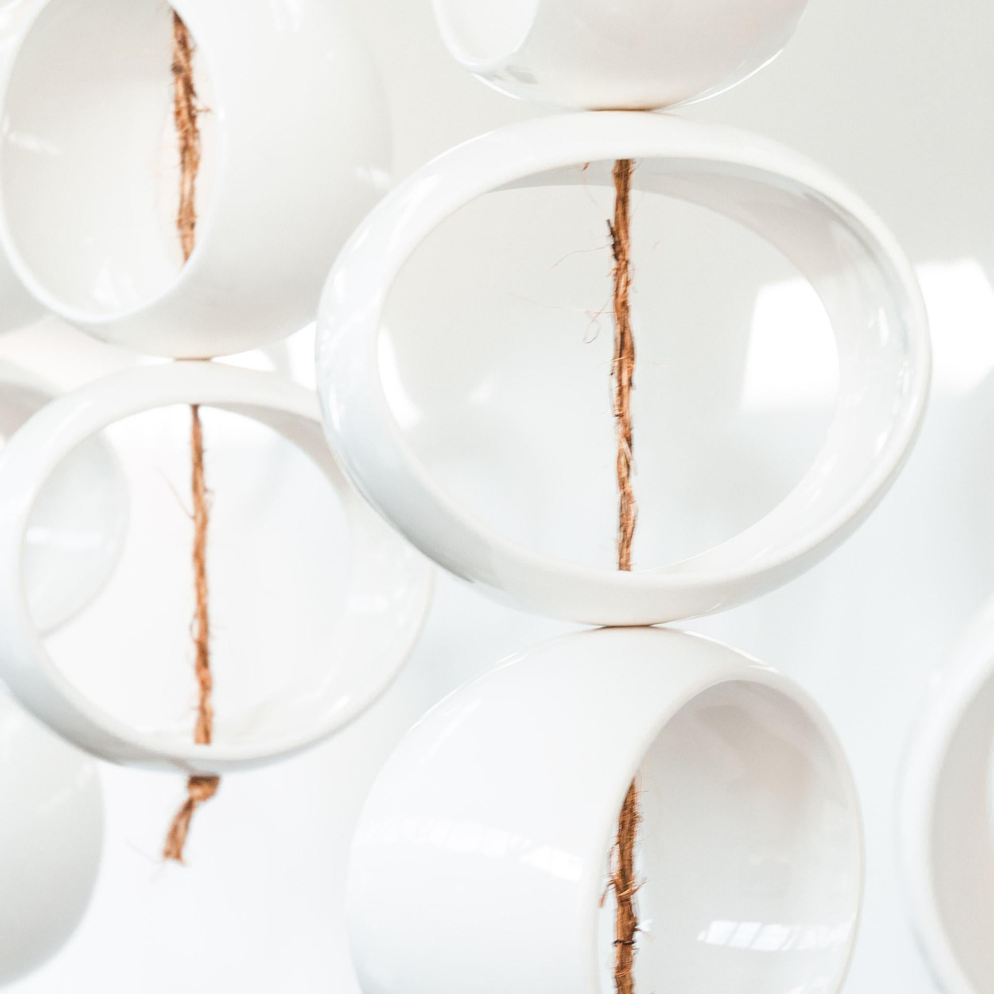 Los puros orbes elípticos de blanco suspendidos por fibras naturales capturan las sombras y lanzan reflejos a través de una habitación. Compuesto por 34 formas de orbe de gres blanco brillante que se sujetan con una cuerda de yute anudada a mano.