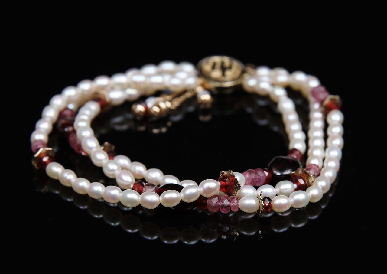 A three-strand bracelet of freshwater pearls, pink tourmaline, rubies, and garnet in a detailed pattern enhanced by 14kt yellow gold spacers and White Orchid Studio's logo clasp. The tassels are of pearl, gold, and ruby. 7.5
