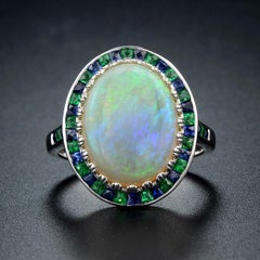 Opale ovale bianco cabochon con smeraldo e zaffiro, anello con incastonatura a raggiera in oro bianco