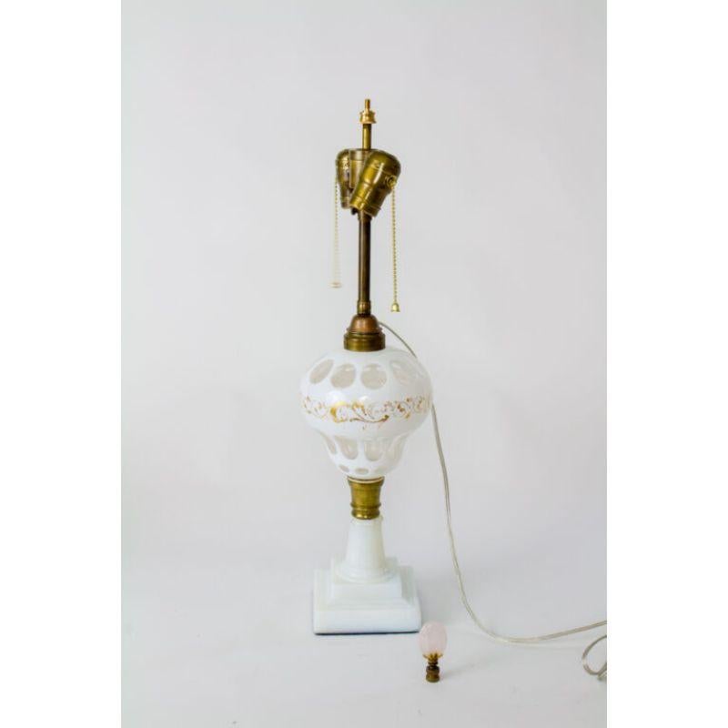 White overlay glass lamp. Attributed to the Boston and Sandwich Glass Company, C. 1860, made in the US. Originally for oil, it has been electrified. The oil font is overlay glass, white to clear, with gold painted details. The base is pressed