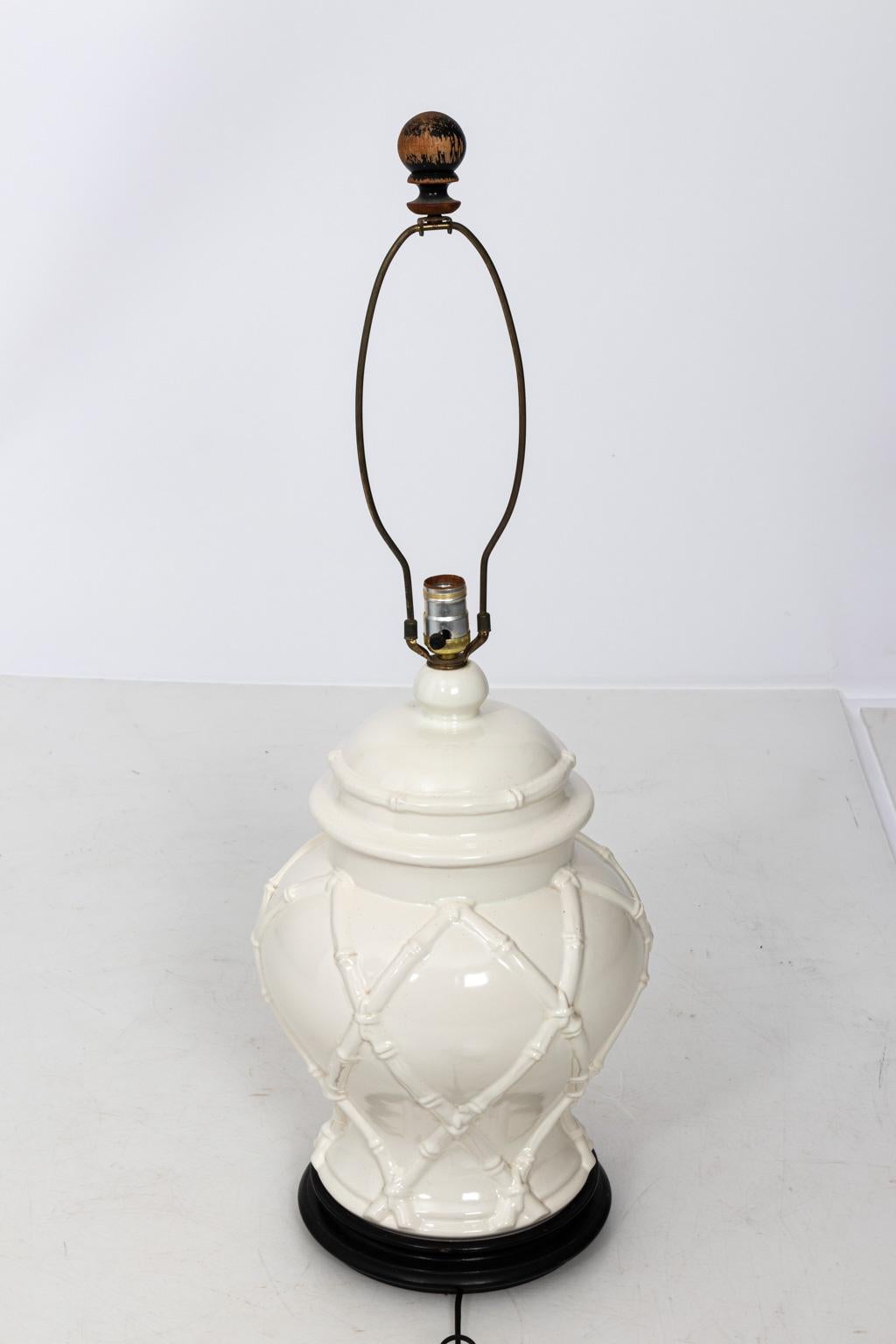 White painted urn shaped ceramic table lamp in the Hollywood Regency style with faux bamboo latticework and original wood finial, circa 20th century. Please note of wear consistent with age. Shade not included. The piece measures 22.00 Inches to the