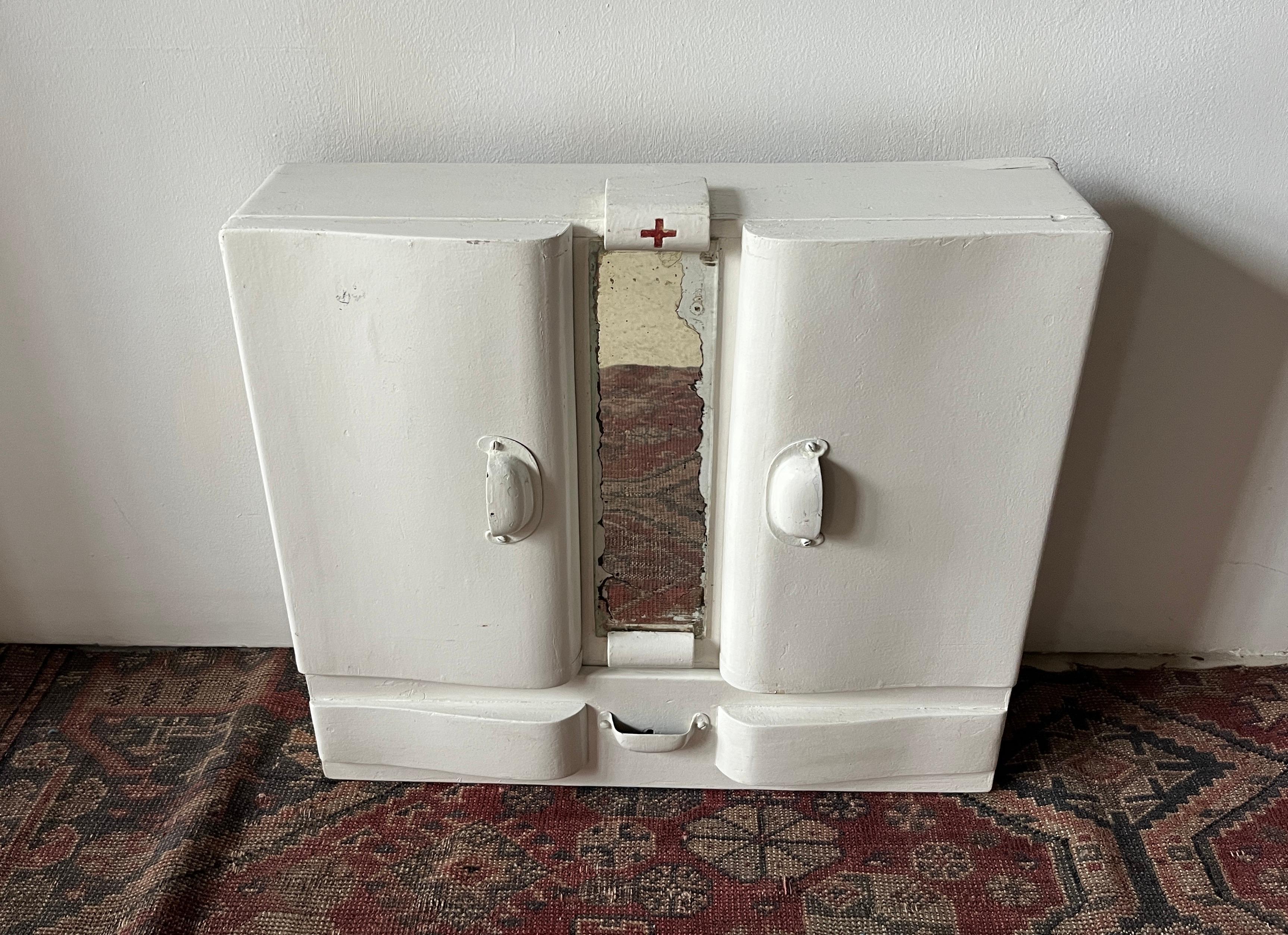White Painted First Aid Wall-Hung Apothecary Cabinet or Medicine Cabinet 

Original unrestored condition. Made of wood with metal hinges and closures. Silver-backed mirror at center with age-appropriate losses. Art deco curved lines to door fronts.