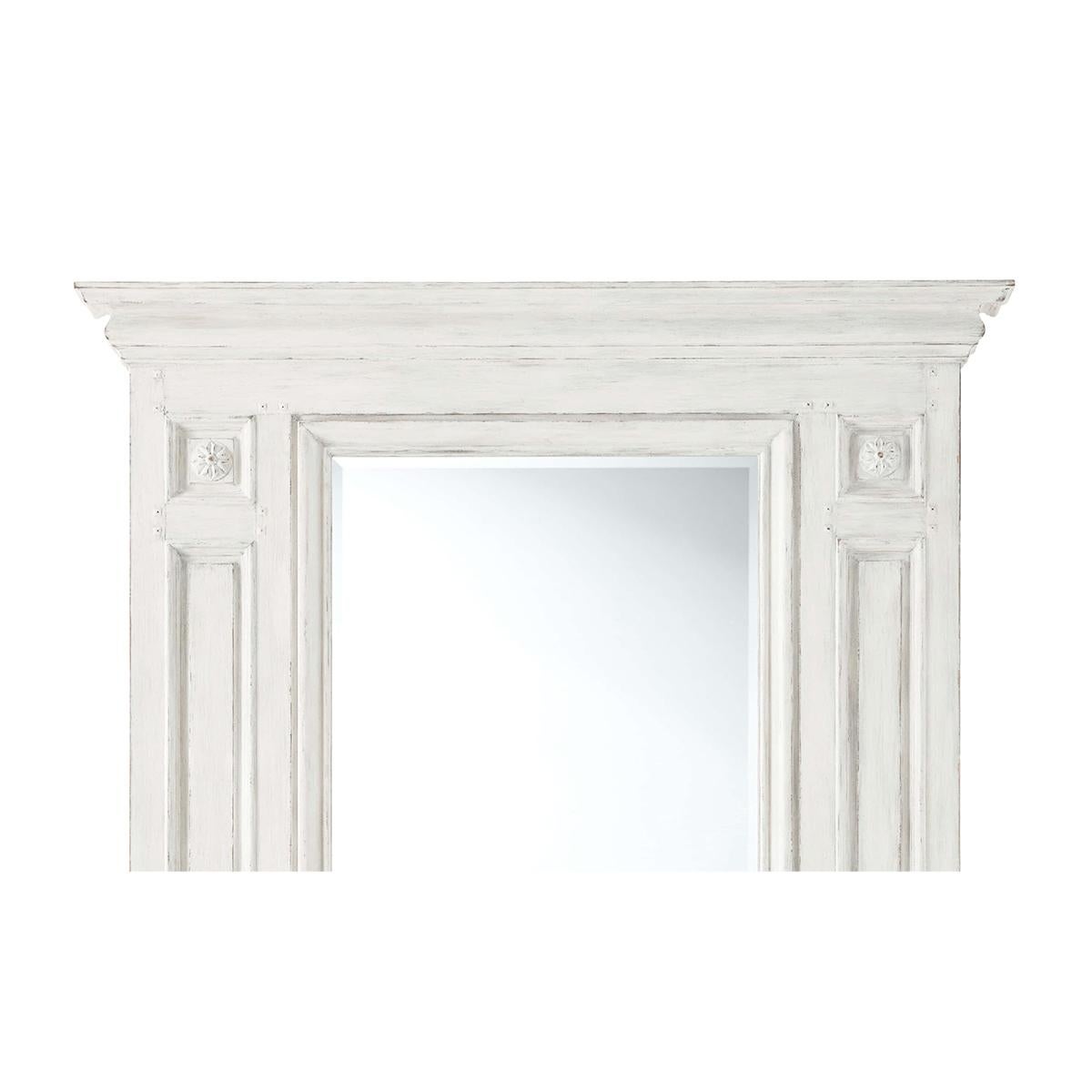 A French neoclassic style white painted and rubbed mirror with a molded cornice, paneled uprights each with flowerhead reliefs and with a beveled mirror. 

Dimensions: 52