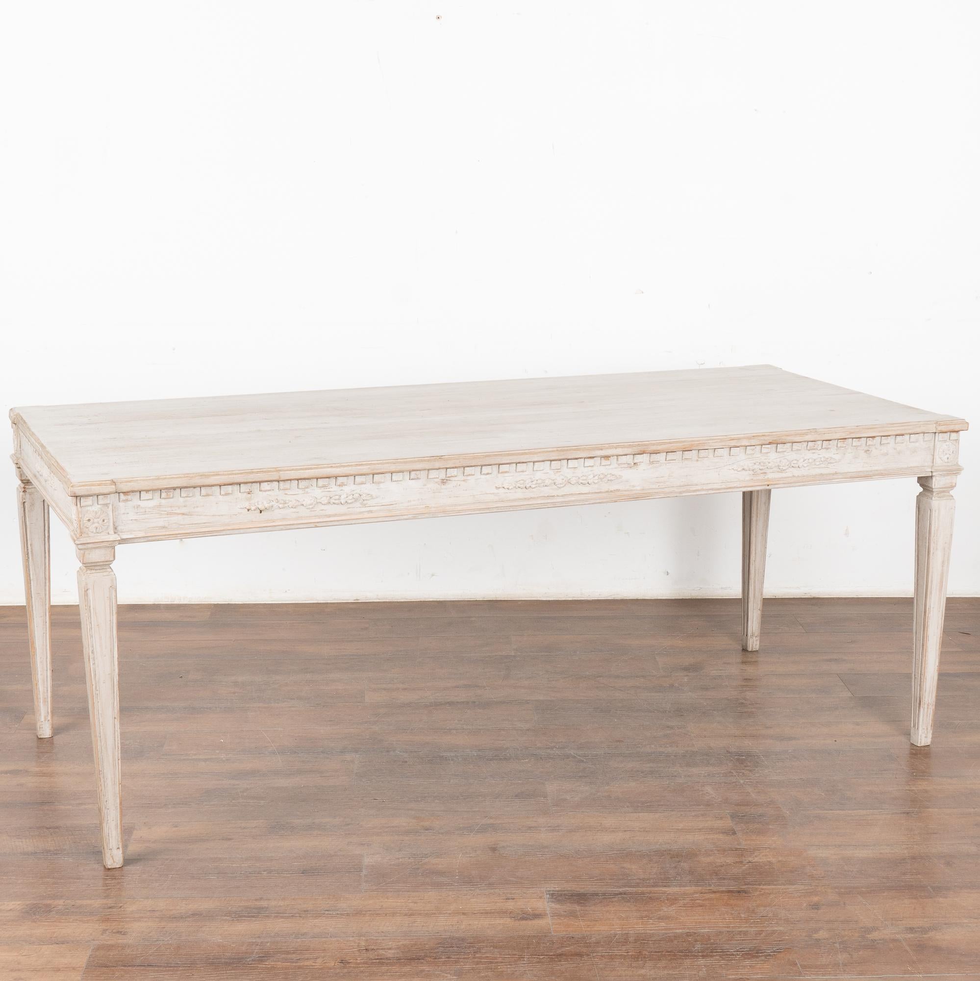 Larga mesa de comedor blanca de estilo Gustaviano de 6,5' con molduras dentiladas y cuatro patas cónicas estriadas que reflejan su estilo campestre sueco.
El nuevo acabado pintado en capas de color blanco antiguo, aplicado profesionalmente, se ha