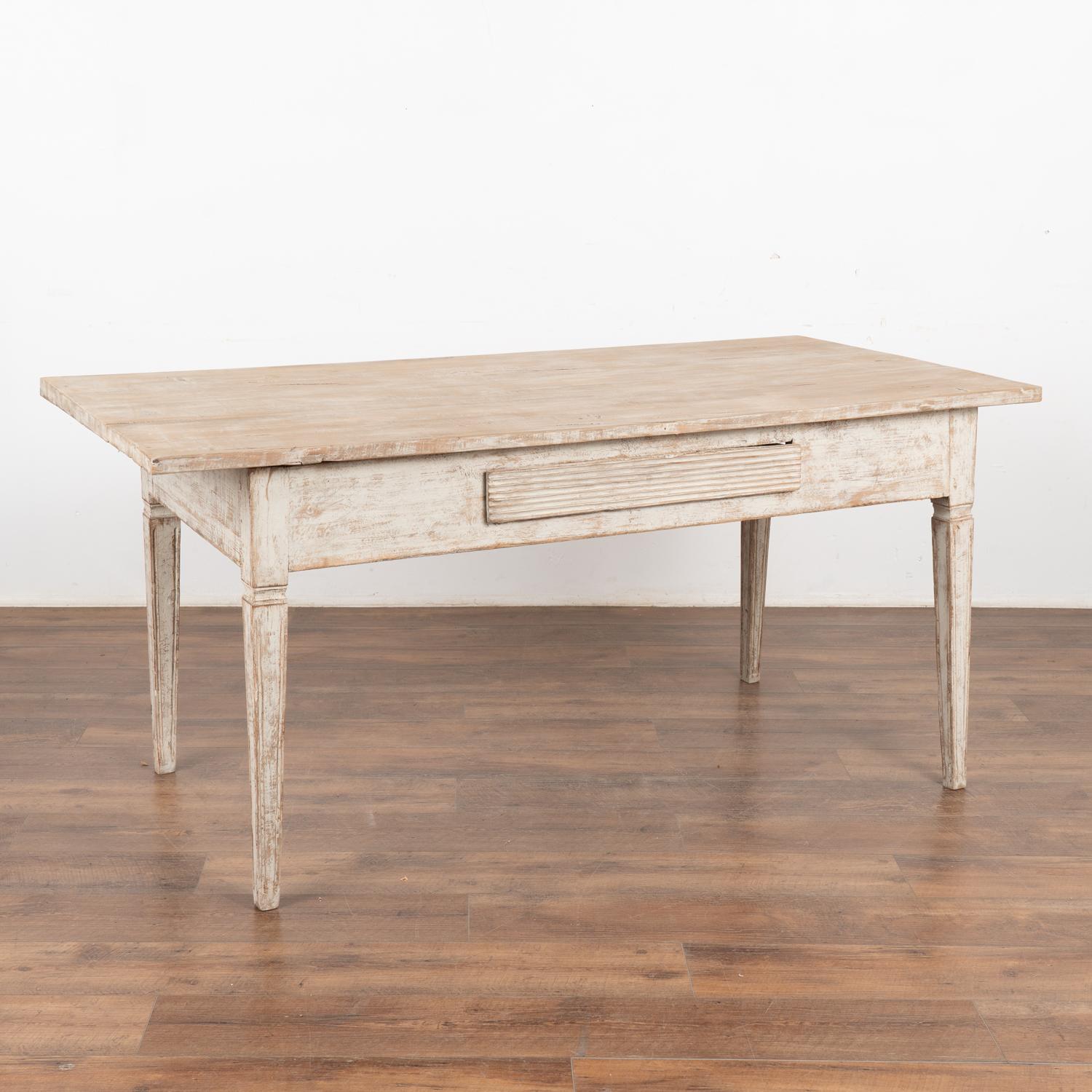 Swedish Gustavian style table with single fluted drawer and tapered legs.
Restored, later professionally painted in layered shades of white now distressed to add to the character and grace of this table that may also serve as a writing desk. 
All