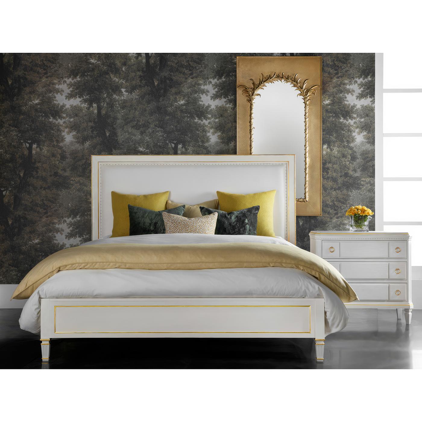 Featuring a performance white linen upholstered headboard framed by an antique white-painted finish with gold-painted accents. The paneled rails and square tapered, and fluted legs pay homage to Gustavian style, bringing a refined and stately charm