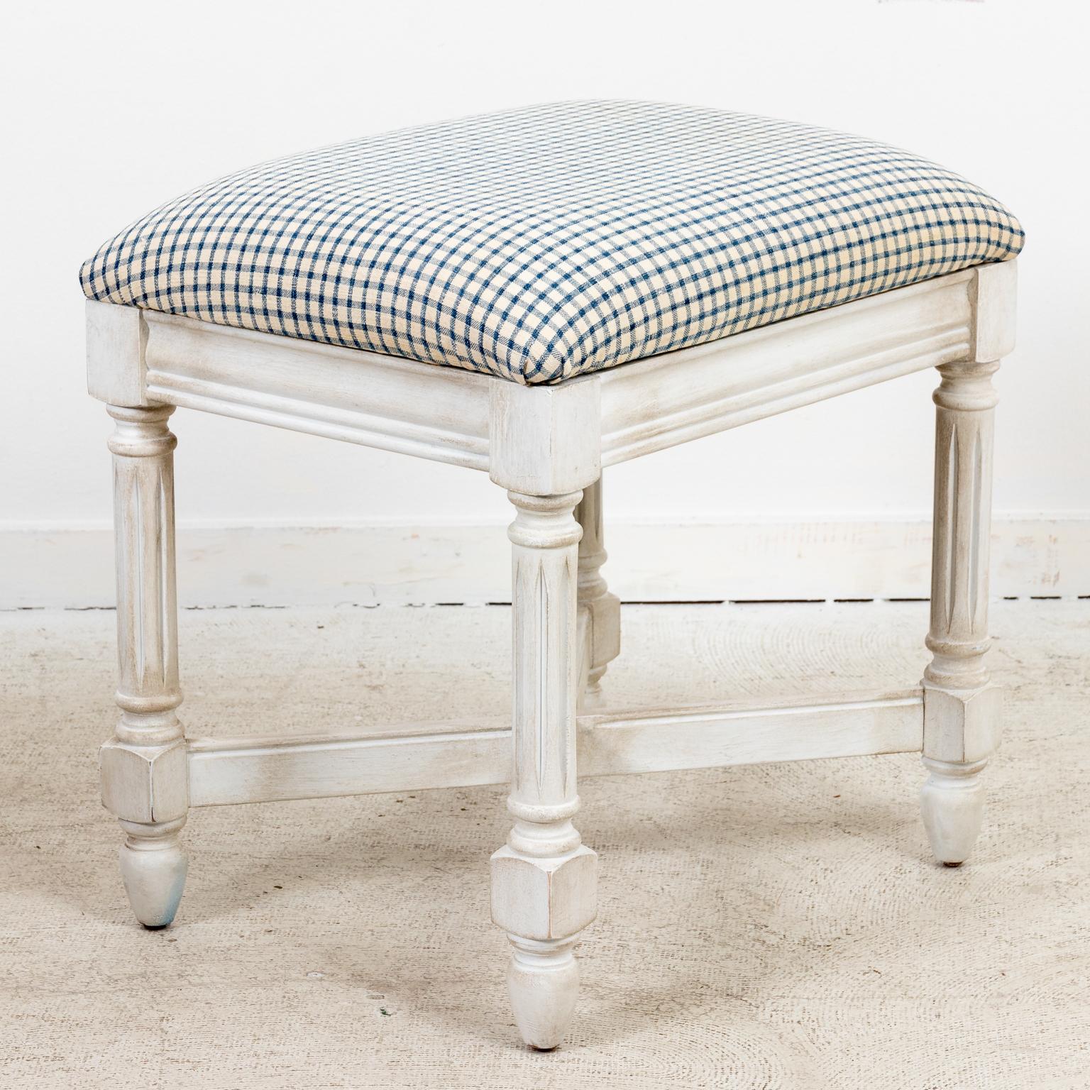 Circa 1970s newly repainted petite Maple bench in the Gustavian style with an x-shaped bottom stretcher and fluted turned legs. Newly re-upholstered with antique homespun cloth in blue and cream check pattern. Made in the United States. Please note