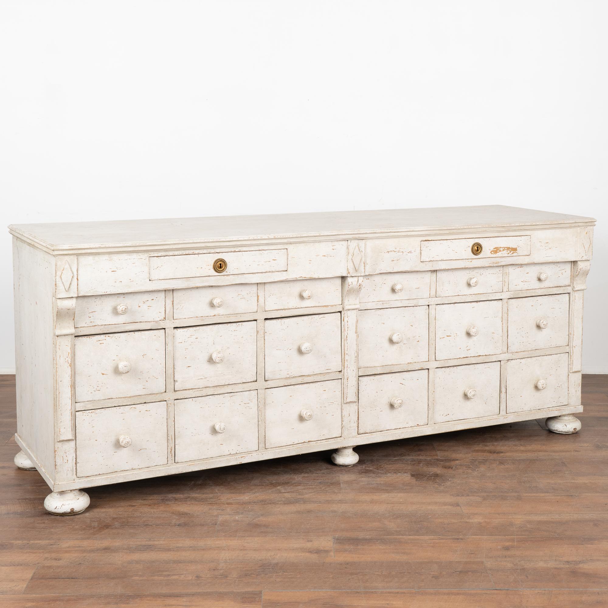 As a free standing counter resting on large bun feet, it will serve well as a modern kitchen island.
This sideboard has been given a professionally applied antique white painted layered finish, lightly distressed to fit the age of the counter