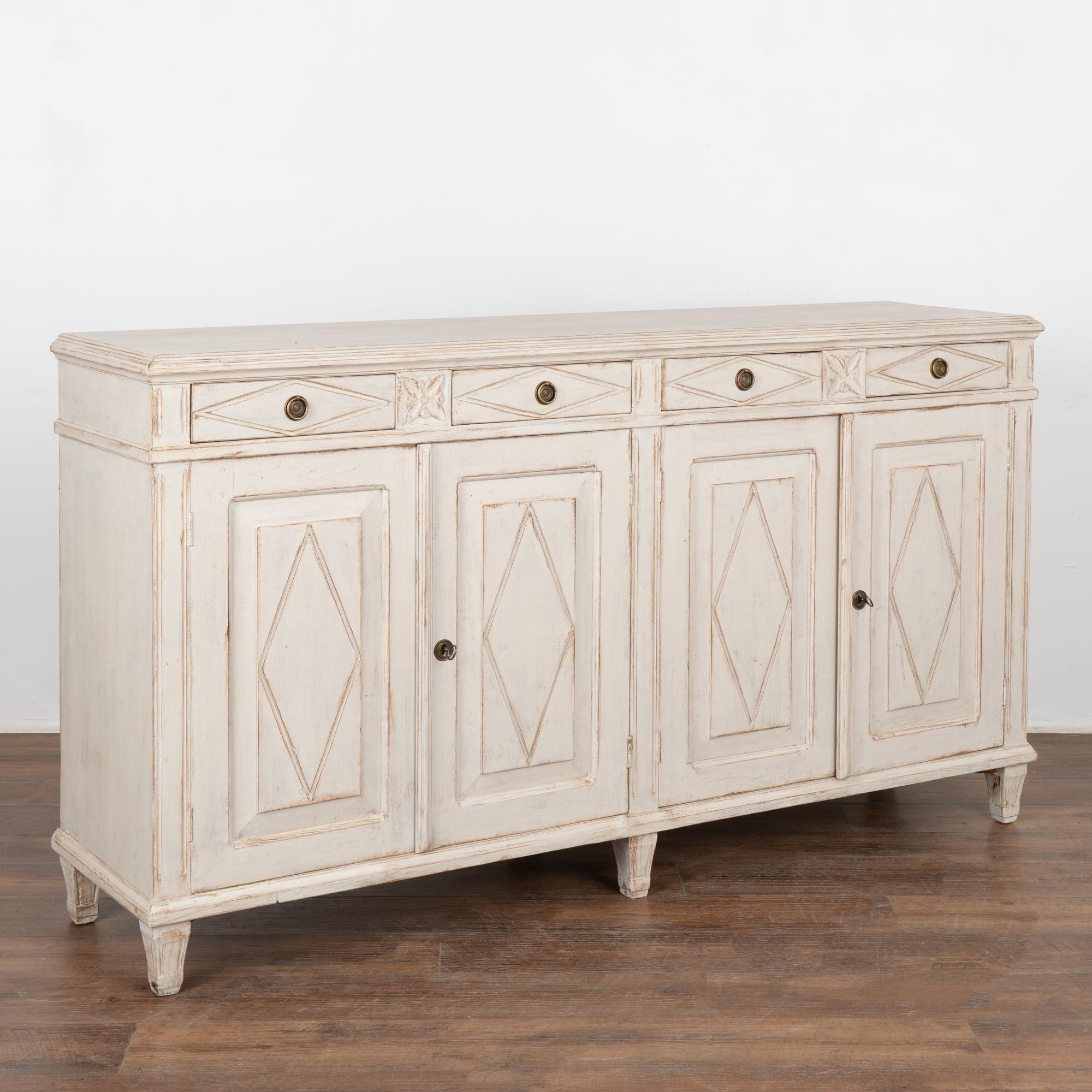 Swedish pine sideboard/buffet with traditional diamond motif carved in drawers and door panels. 
Four drawers over four cabinet doors, one long interior shelf.
Restored, later professionally painted in layered shades of white and lightly distressed